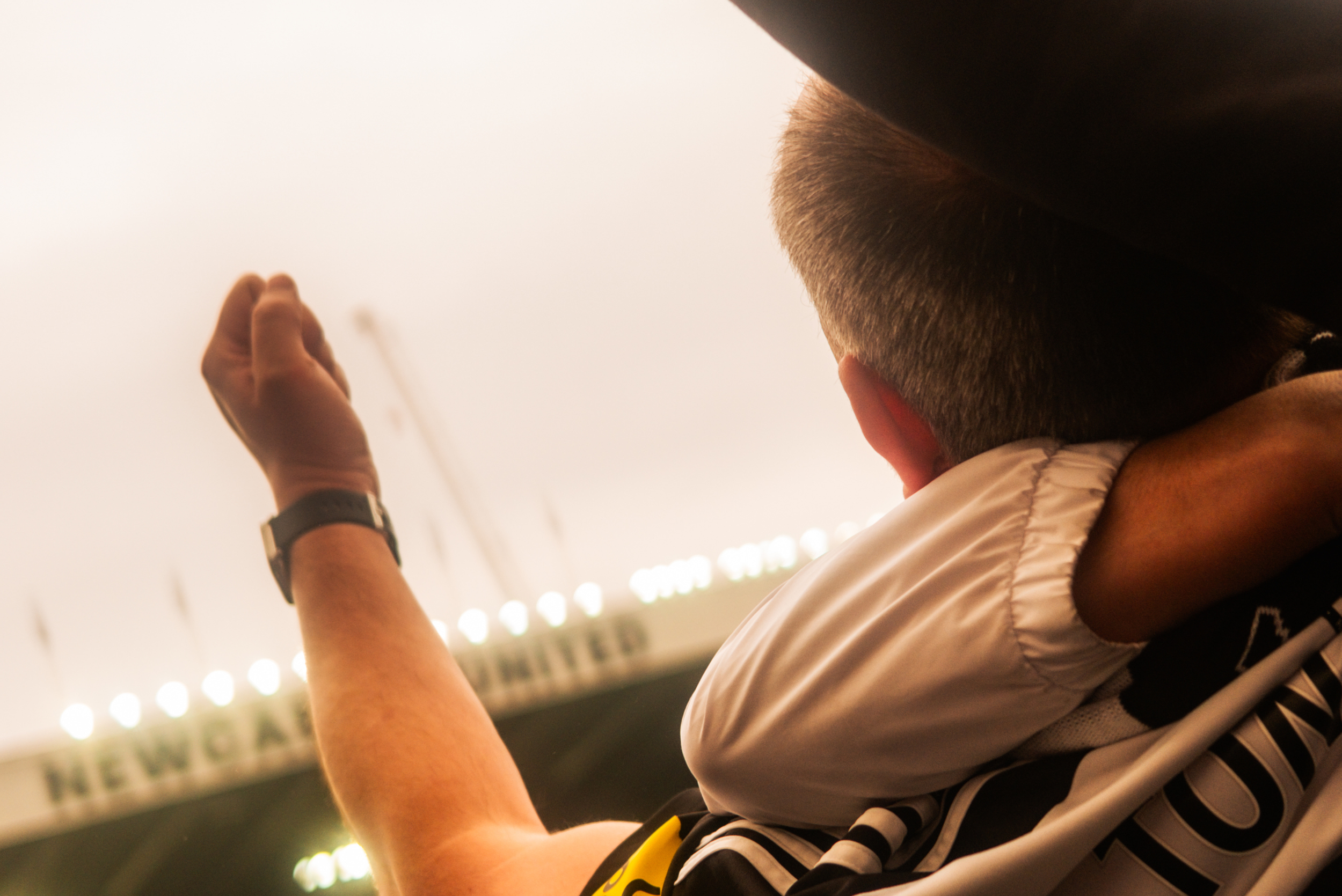 A person wearing a striped black and white shirt and a black cap is holding a small object with a hand. The background features bright lights and signs, indicating an indoor setting or a place with decorative lighting.
