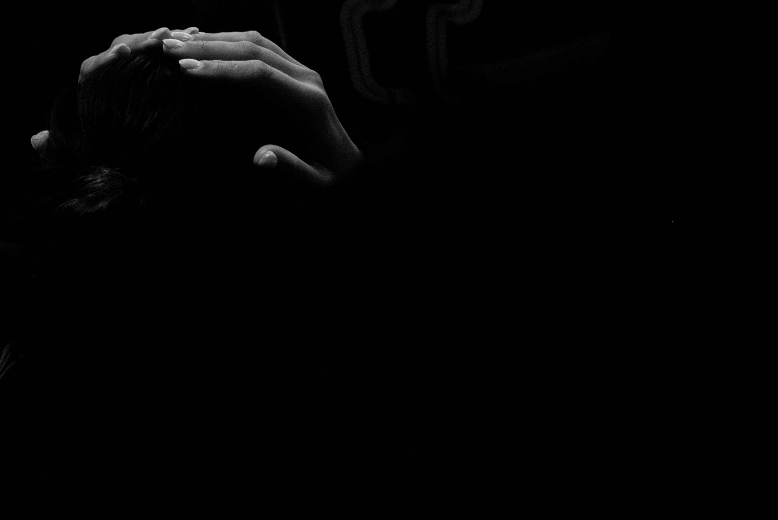 A black and white photo of a person's head with hands covering the face, in a dark setting.