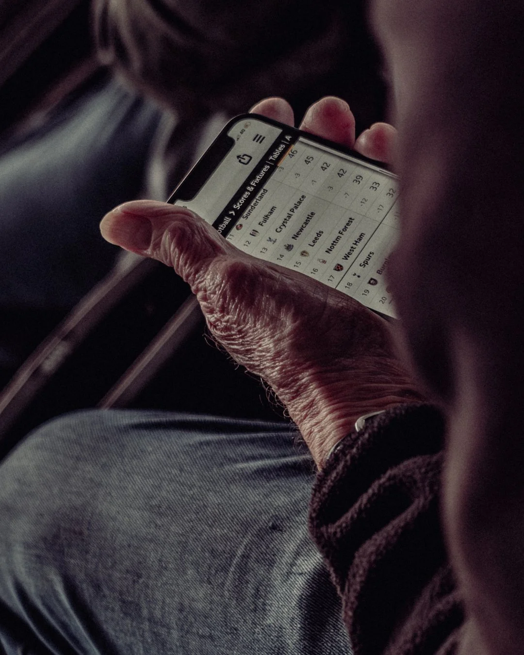 Person holding a smartphone displaying a table with football scores, including teams like Sunderland, Fulham, Crystal Palace, Newcastle, Leeds, Nottingham Forest, West Ham, Tottenham, and Burnley.