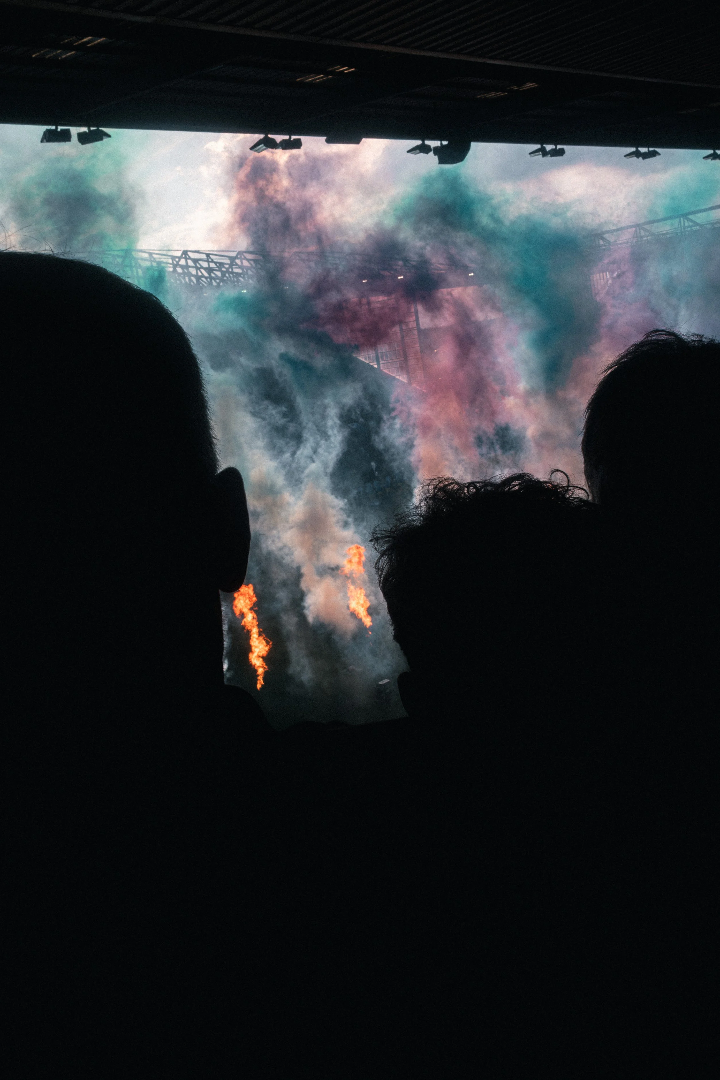 Silhouette of people in front of a colorful smoke display with flames visible at the bottom.
