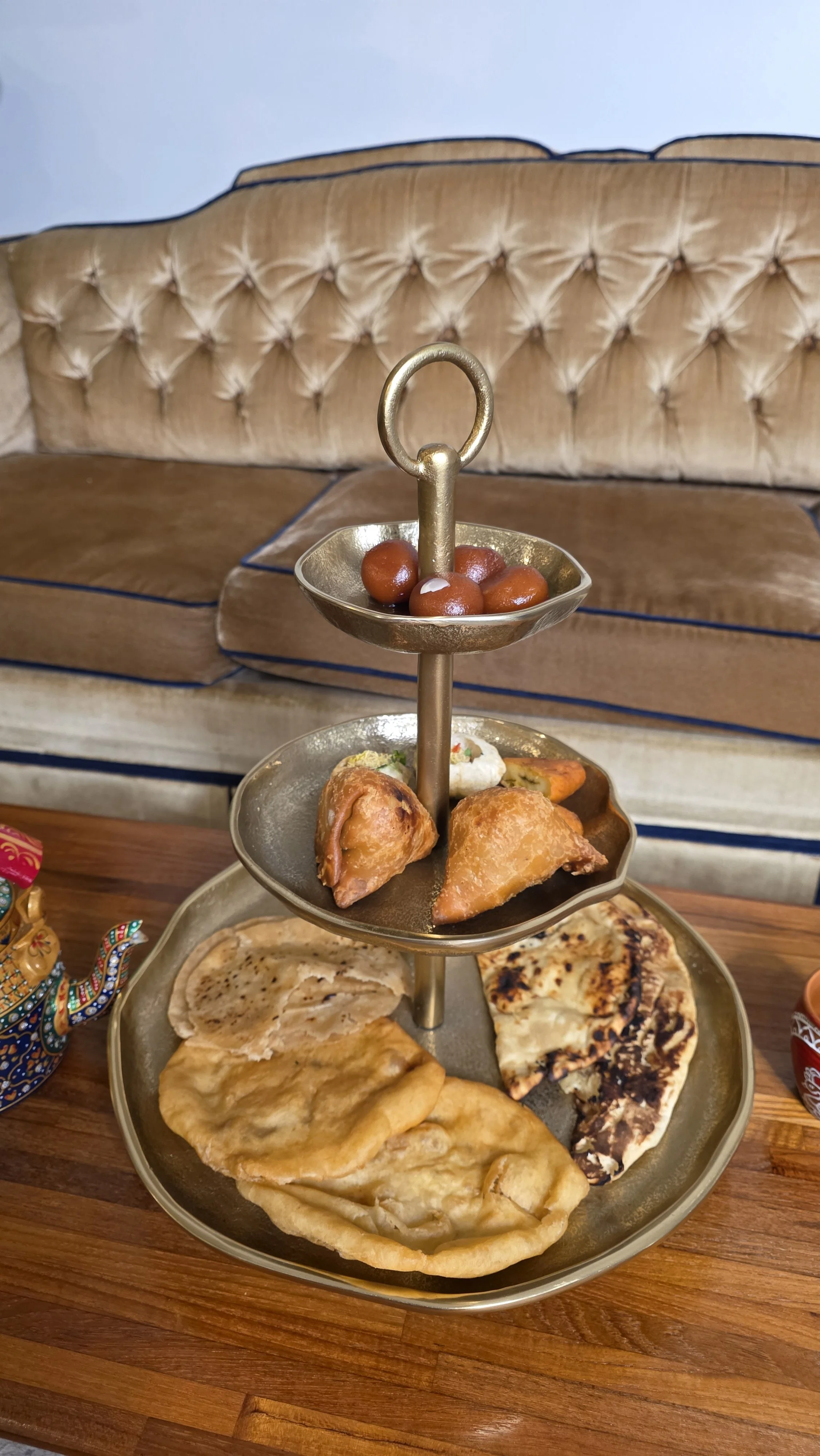 Luxe Tea product photo depicting three-tiered tea tower of roti, naan, samosas, pani puri, and gulab jamun
