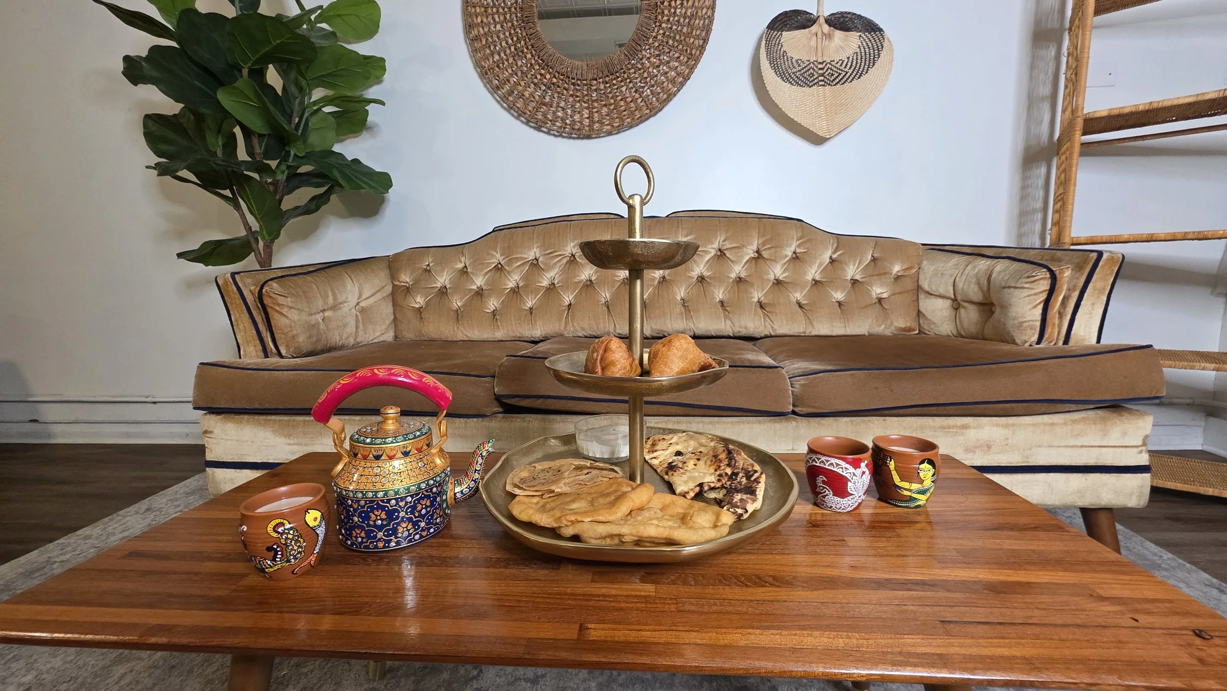 Luxe Tea product photo depicting a three-tier tea tower of Indian dishes, an ornate hand painted teapot, and hand painted clay cups filled with chai
