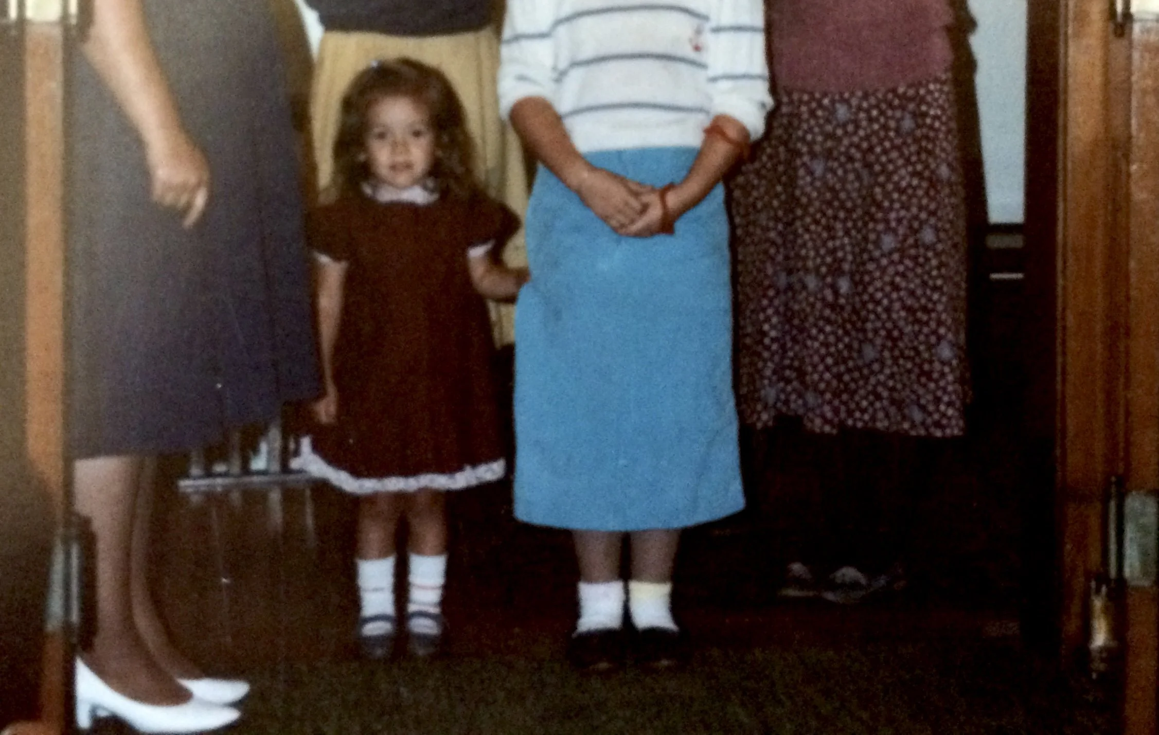 Sorina Noire as a young girl in a burgundy dress, standing among women at a family gathering.