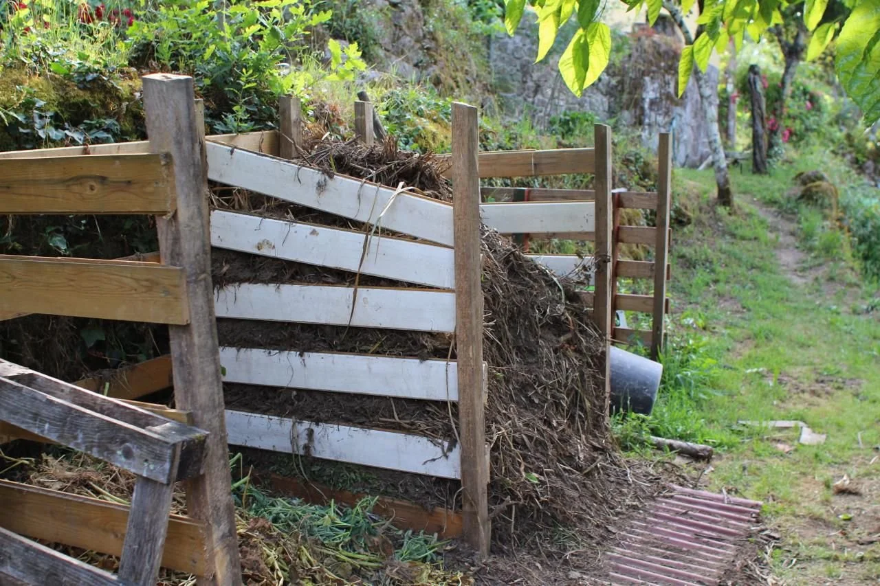 A wooden fence partially buried with dirt and plant debris on a hillside next to a garden path.
