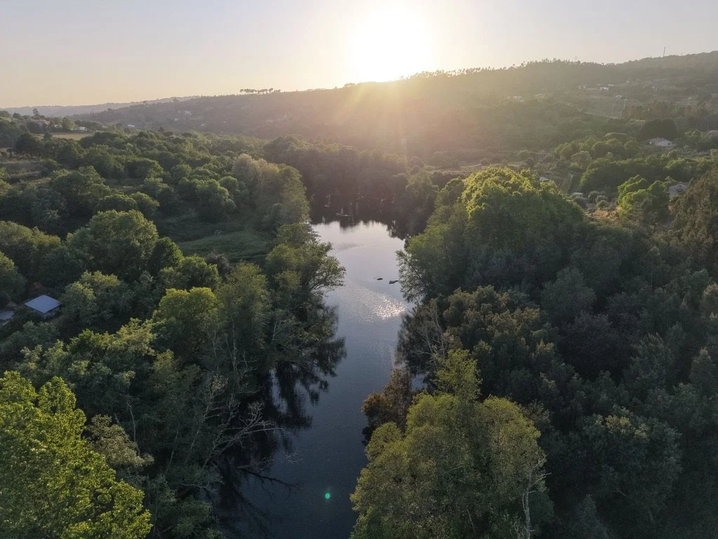 Aerial view of a river flowing through a densely wooded valley with the sun setting in the background.