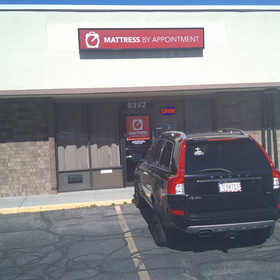 MBA-SLC's owner's vehicle parked in 8400 Plaza parking lot, near the MBA-SLC entrance, proudly displaying the Christian rear window sticker and "In God We Trust" Utah state license plate with American flag license plate frame.