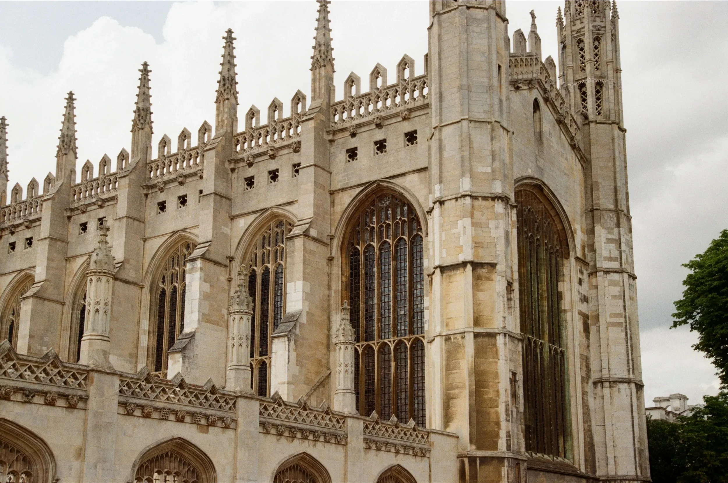 Exterior of a historic Gothic cathedral with ornate stone architecture, large stained glass windows, and tall spires reaching into the cloudy sky.