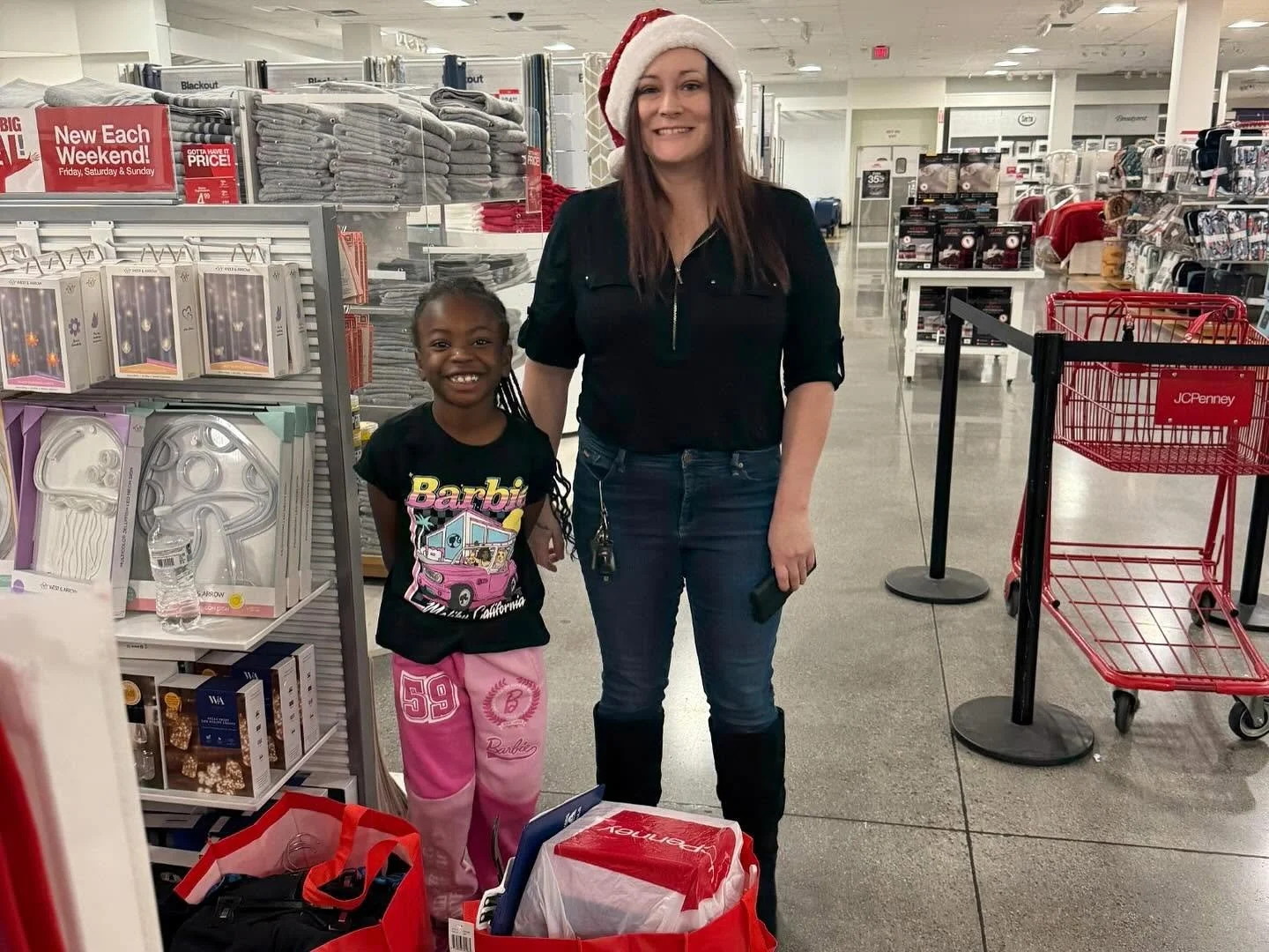 A woman wearing a Santa hat and a young girl standing inside a store near holiday decorations and shopping carts.