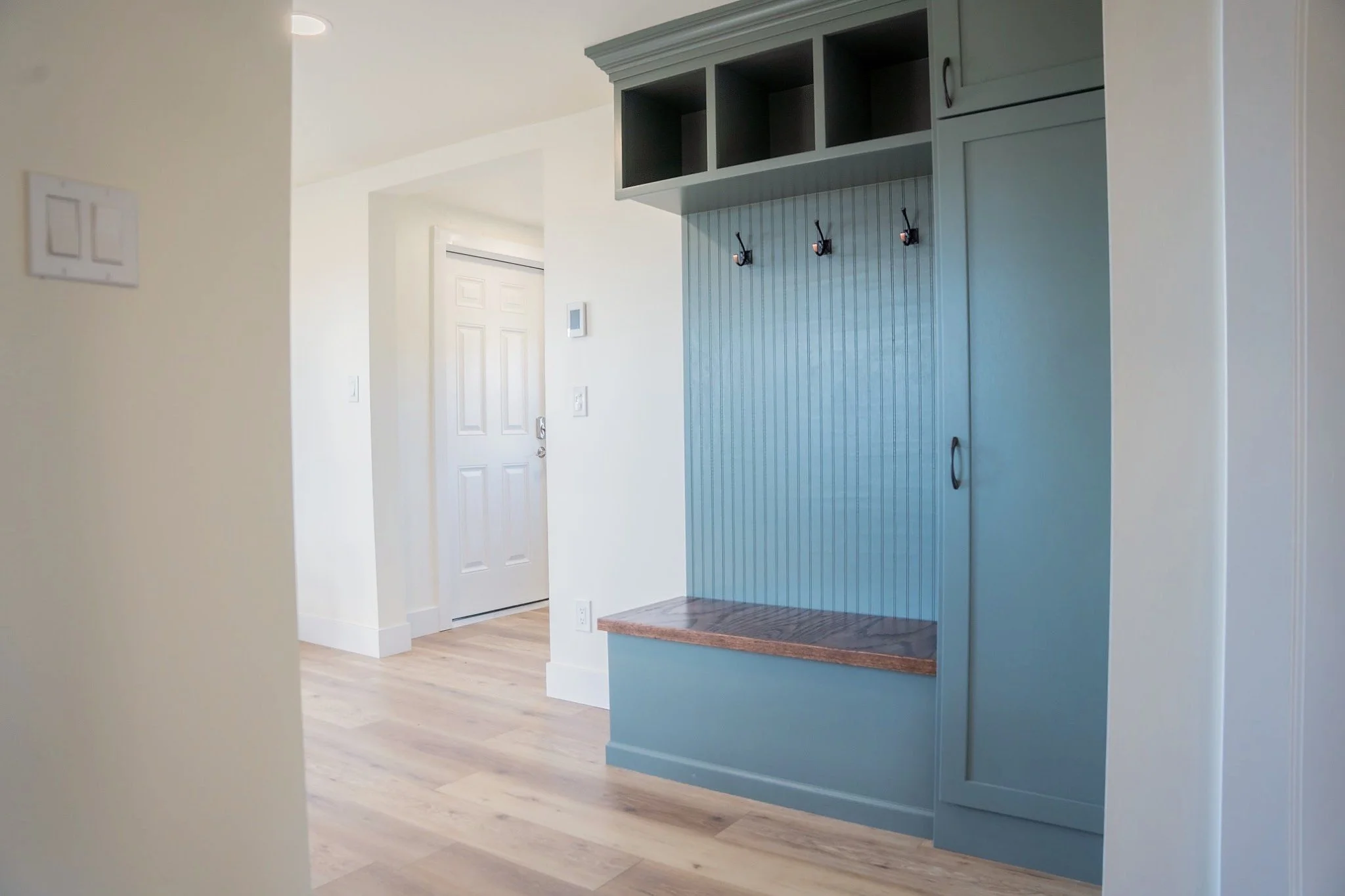 Custom-built and painted mudroom storage with a wood bench, coat hooks, overhead cubbies, and shoe storage.