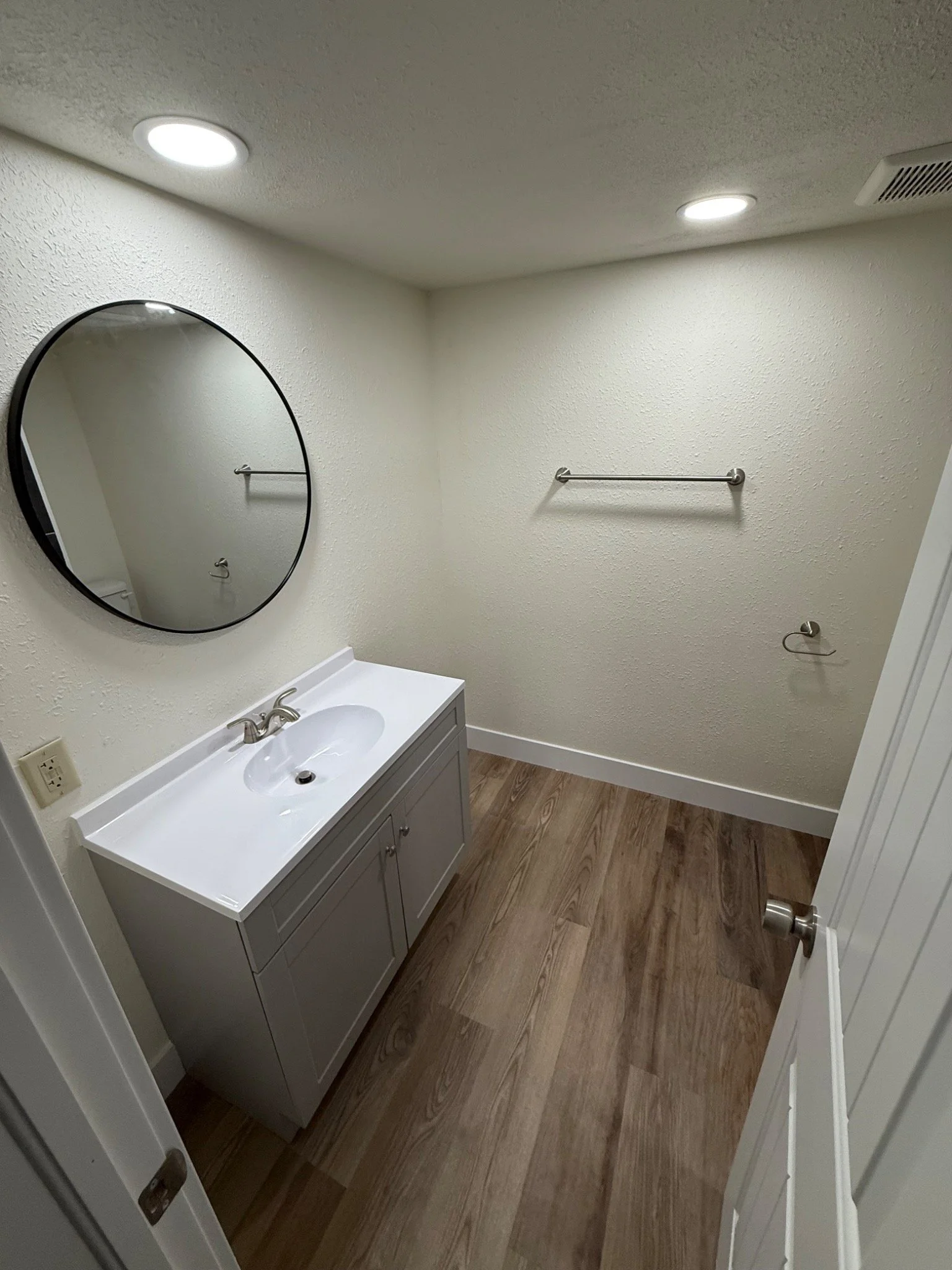 Completed basement bathroom with vanity, round mirror, finished walls, and flooring.