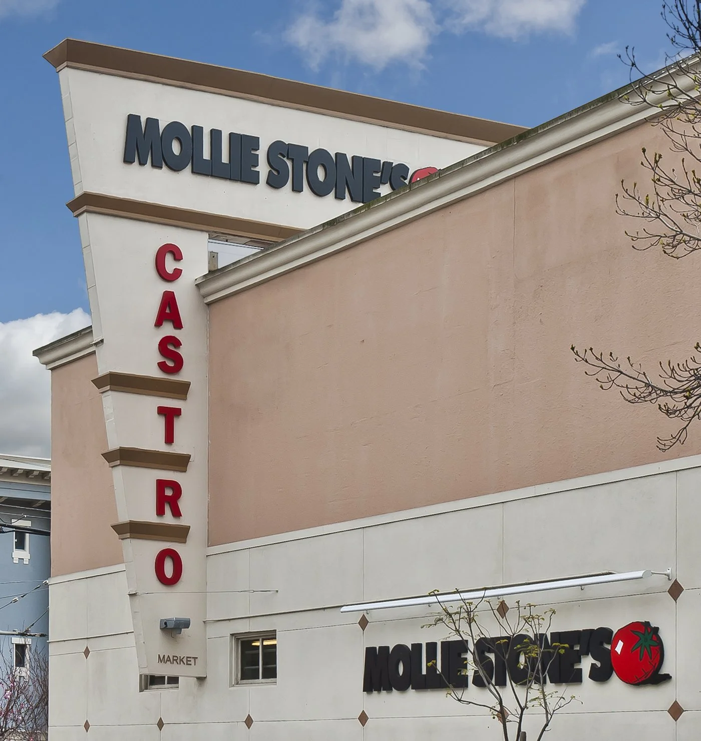 Exterior of Mollie Stone's grocery store with a sign for a deli counter and a tomato logo on the building wall
