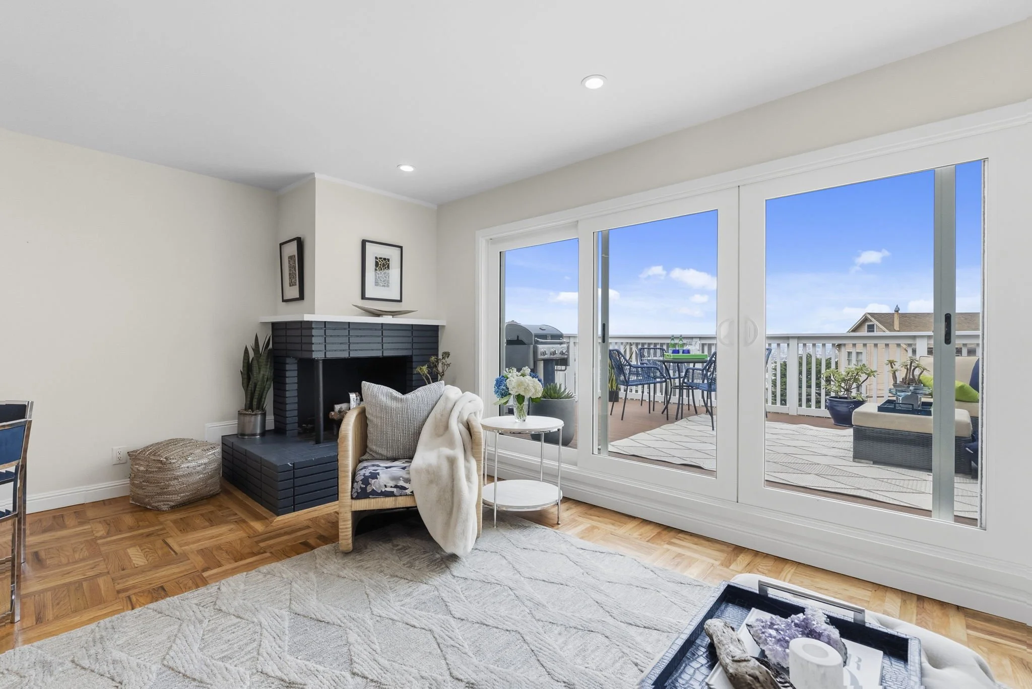 Living room with sliding glass door leading to a balcony, a fireplace, and seating area with a chair and side table, decorated with plants and artwork.