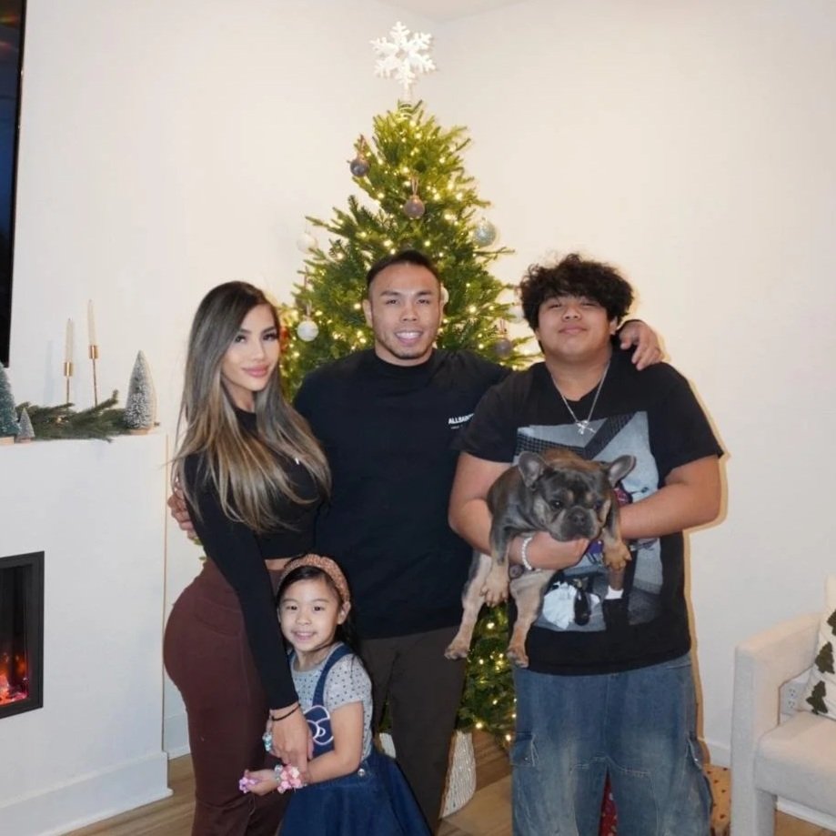 A family of four with a dog in front of a decorated Christmas tree, smiling inside a living room.