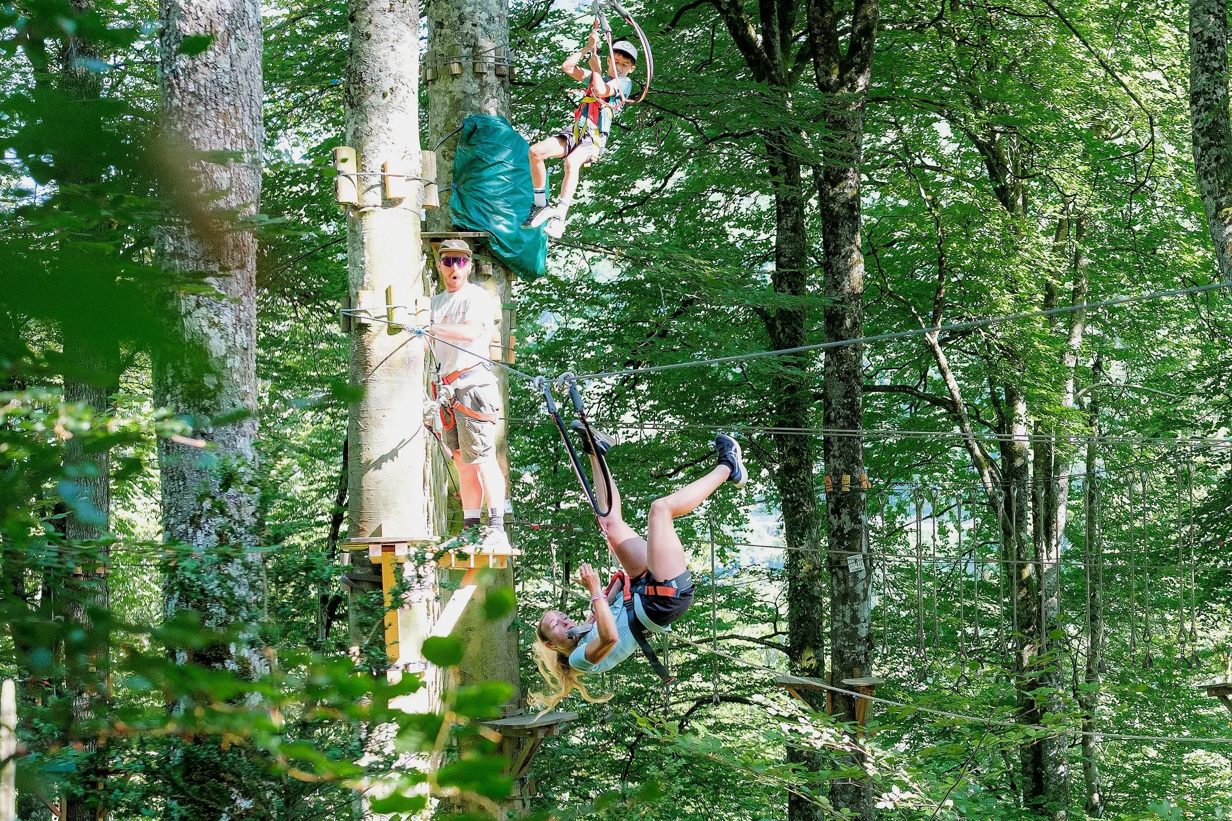 Des personnes faisant de la tyrolienne dans une forêt dense, suspendues à des câbles et portant un équipement de sécurité, entourées d'arbres verts.