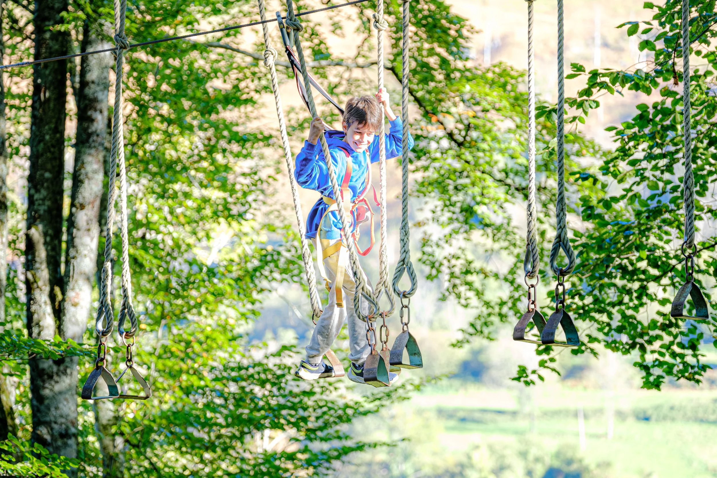 Un garçon en plein air sur une tyrolienne traverse une forêt en souriant.