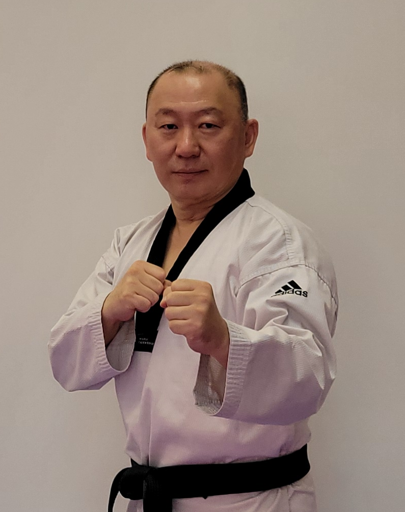 Man in a taekwondo uniform posing with fists up in a kicking stance.