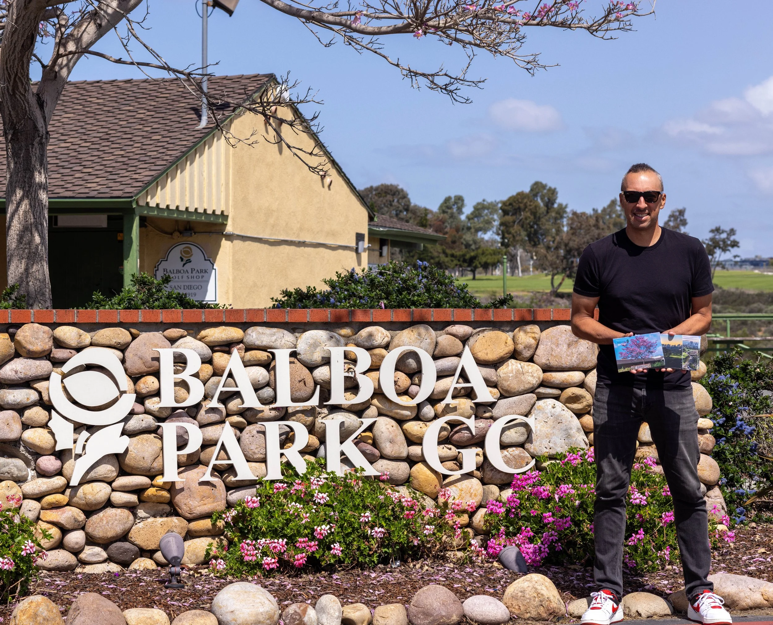Lucky Lopez standing in front of the Balboa Golf Course club house showcasing the drone images of the golf course that sell as post cards in the pro shop.