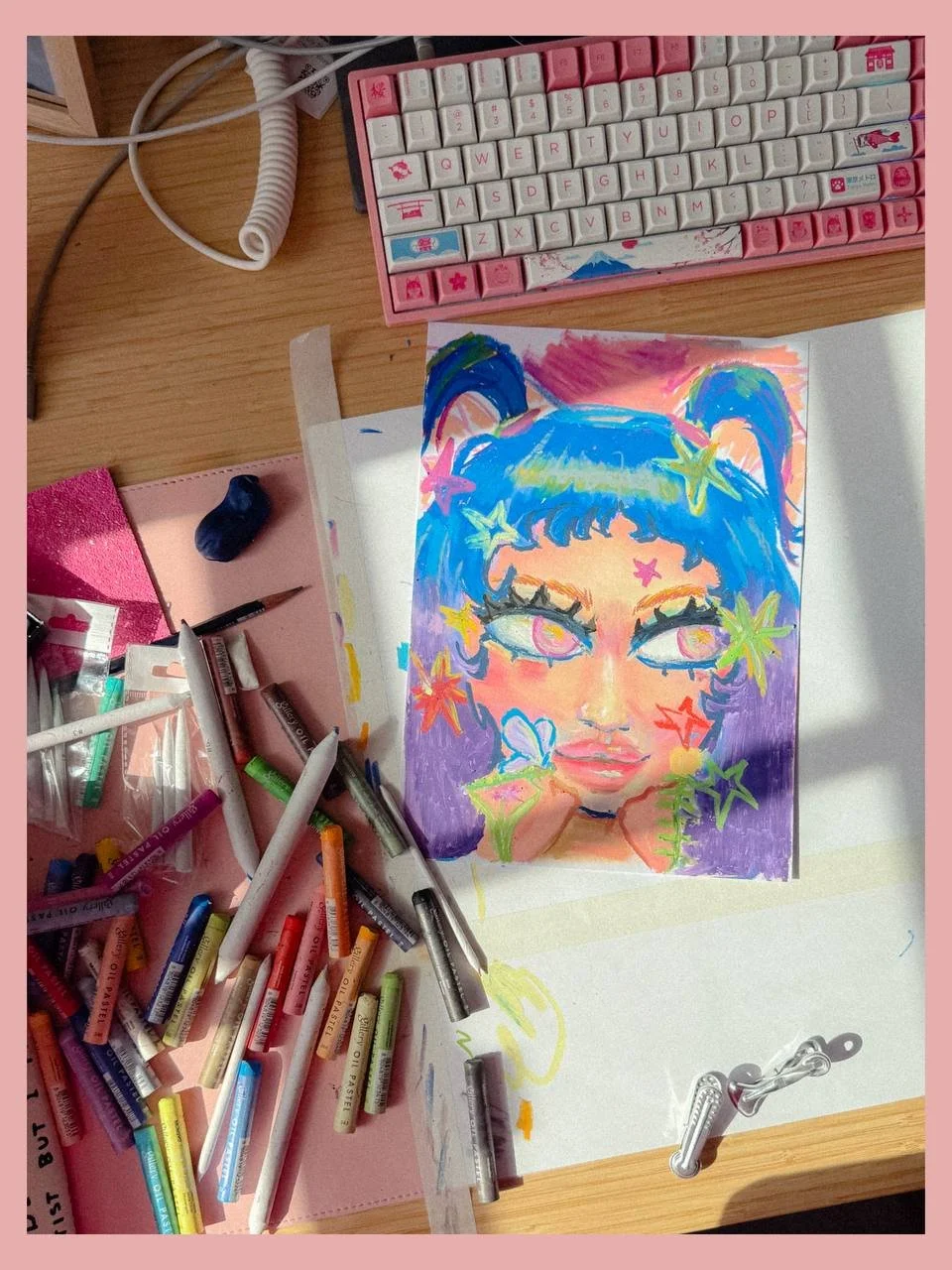 Colorful illustration of a girl with blue hair styled in pigtails, surrounded by multicolored stars, on a desk with art supplies and a pink keyboard.