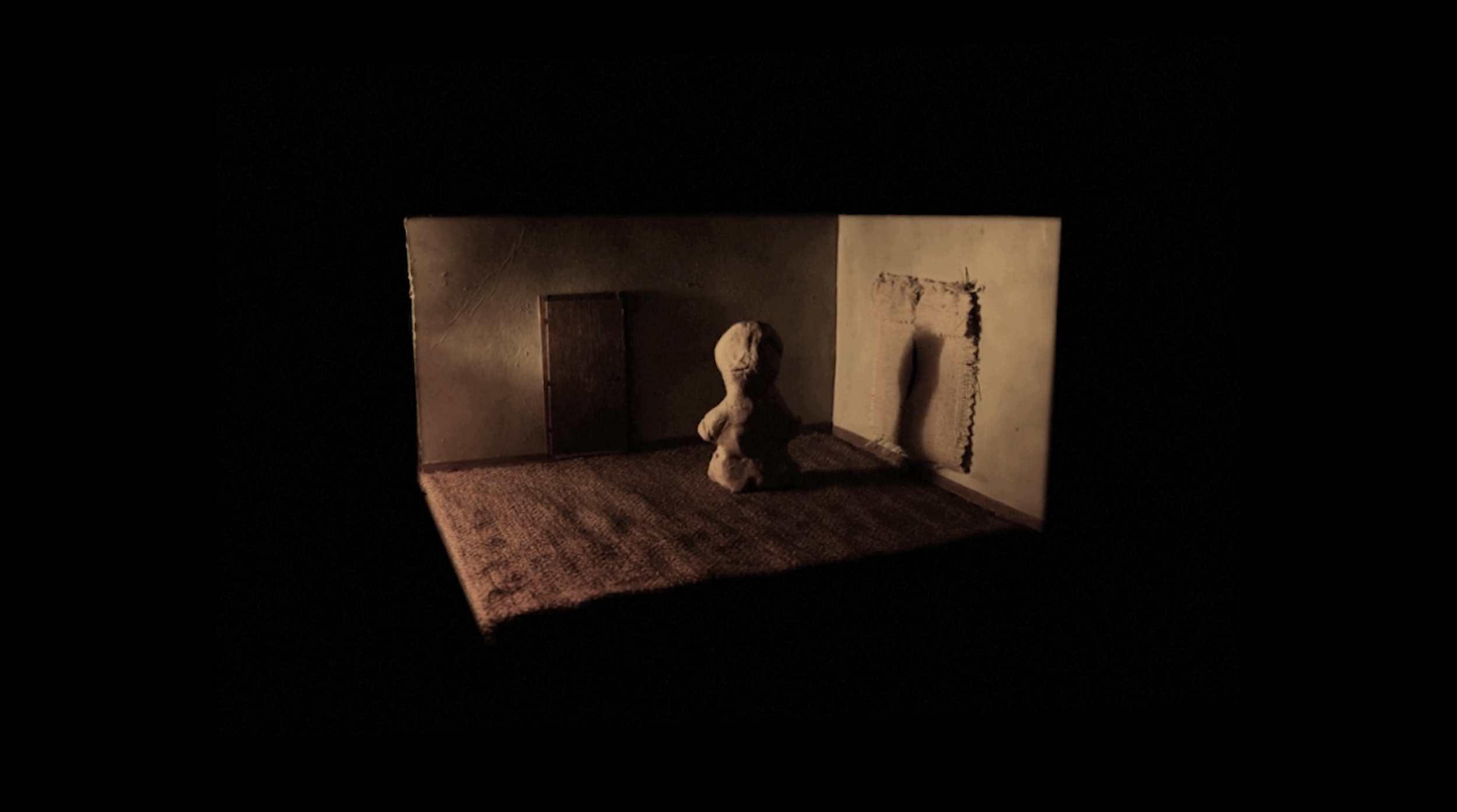 A miniature diorama with a small chair, a sculpture of a headless figure, and a partially destroyed wall segment, all illuminated in a dark space.