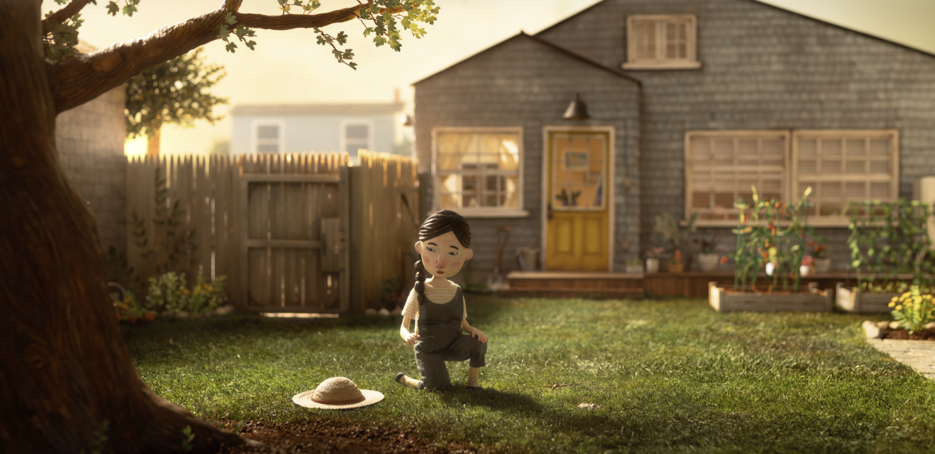 A small doll kneeling on the grass in a backyard during sunset, with a straw hat beside her, a tree to the left, and a house with a yellow door and garden beds in the background.