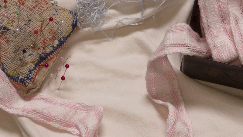 Sewing materials including pins, a pincushion, fabric, and a wooden ruler on a white surface.