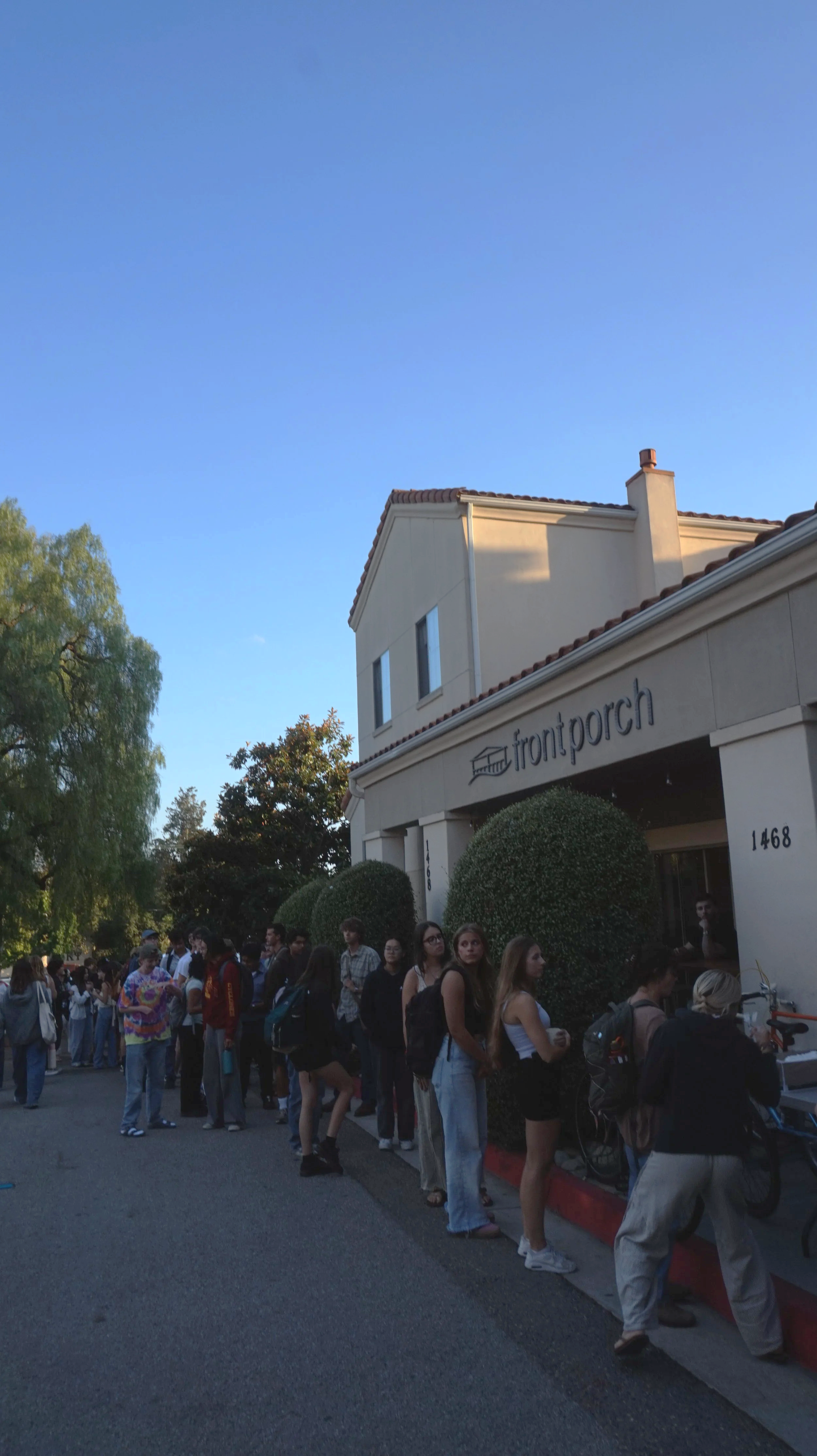 Line of people waiting outside a building with a sign that reads 'front porch'.