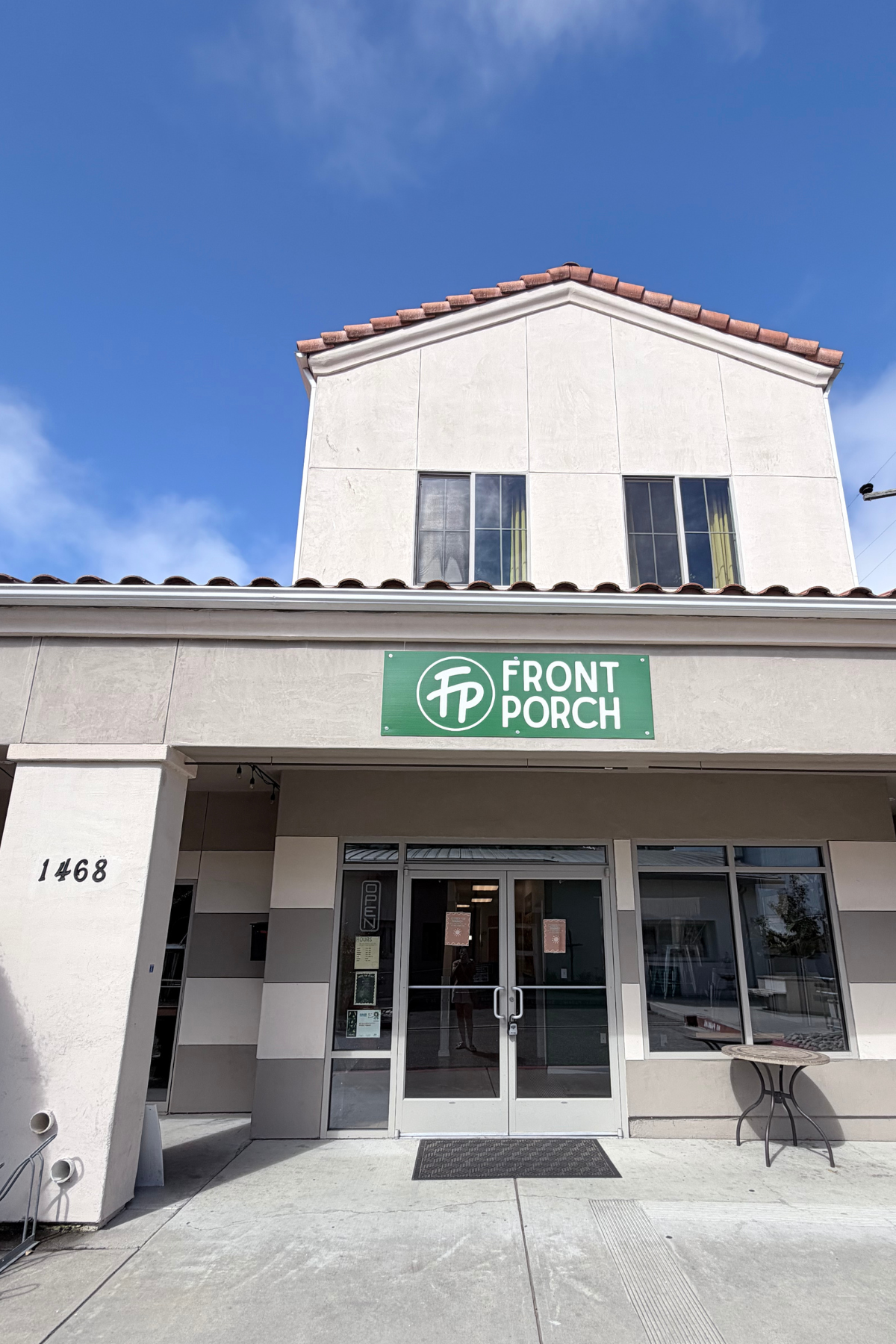 Front view of a building with a green sign reading 'FP Front Porch,' a white exterior, large glass double doors, and the street number 1468 on the left side.
