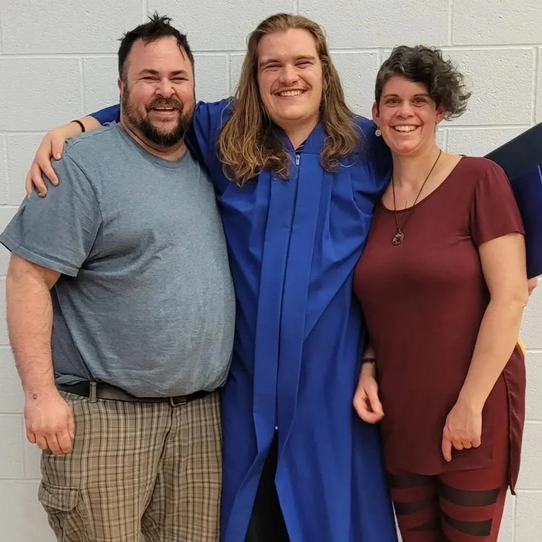 Three people standing together smiling, one in a graduation gown.