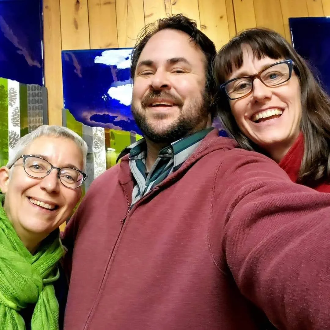 Four smiling friends taking a selfie indoors, with wooden panel walls and colorful artwork in the background.