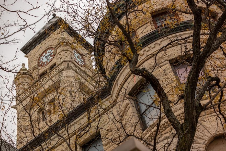 Ghost Sedgewick County Historical Museum. Downtown Wichita. A historic building with a clock tower, beige stone facade, decorative architectural details, and leafless tree branches in the foreground.
