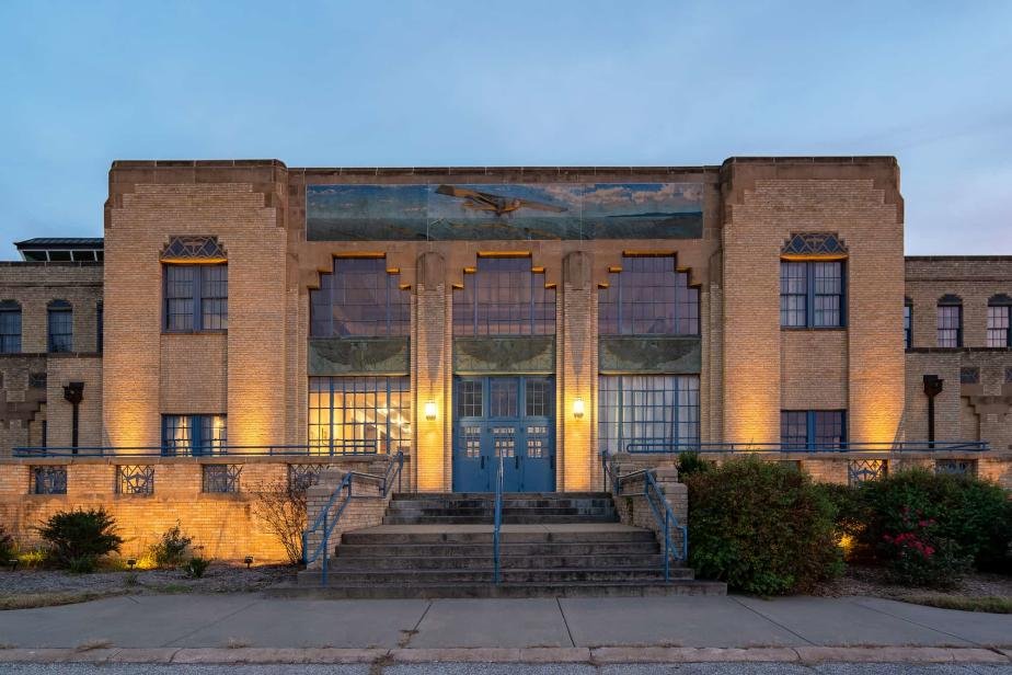 Ghost tours Simmons Bank in Wichita Kansas. Haunted Location. A historic brick building with large stained glass windows, front steps, and decorative lights illuminating it at dusk.