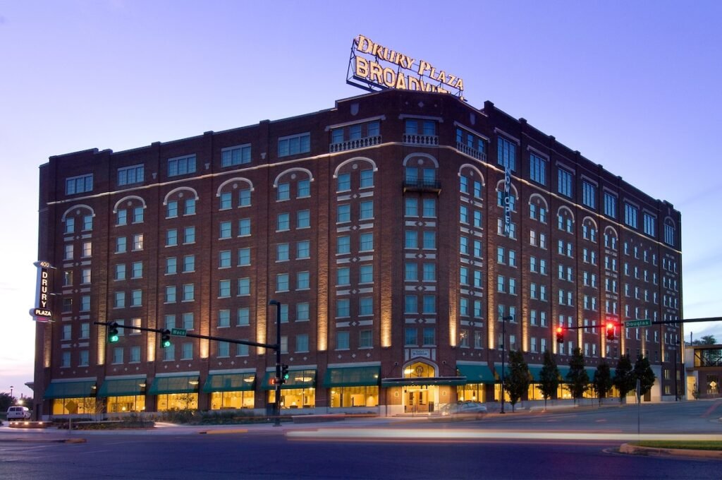 Most Haunted Hotel in Wichita. Ghost activity. large brick hotel building at dusk with illuminated signs reading 'Dreary Plaza' and 'Broadway'. The building has multiple windows and a neon "Open" sign.