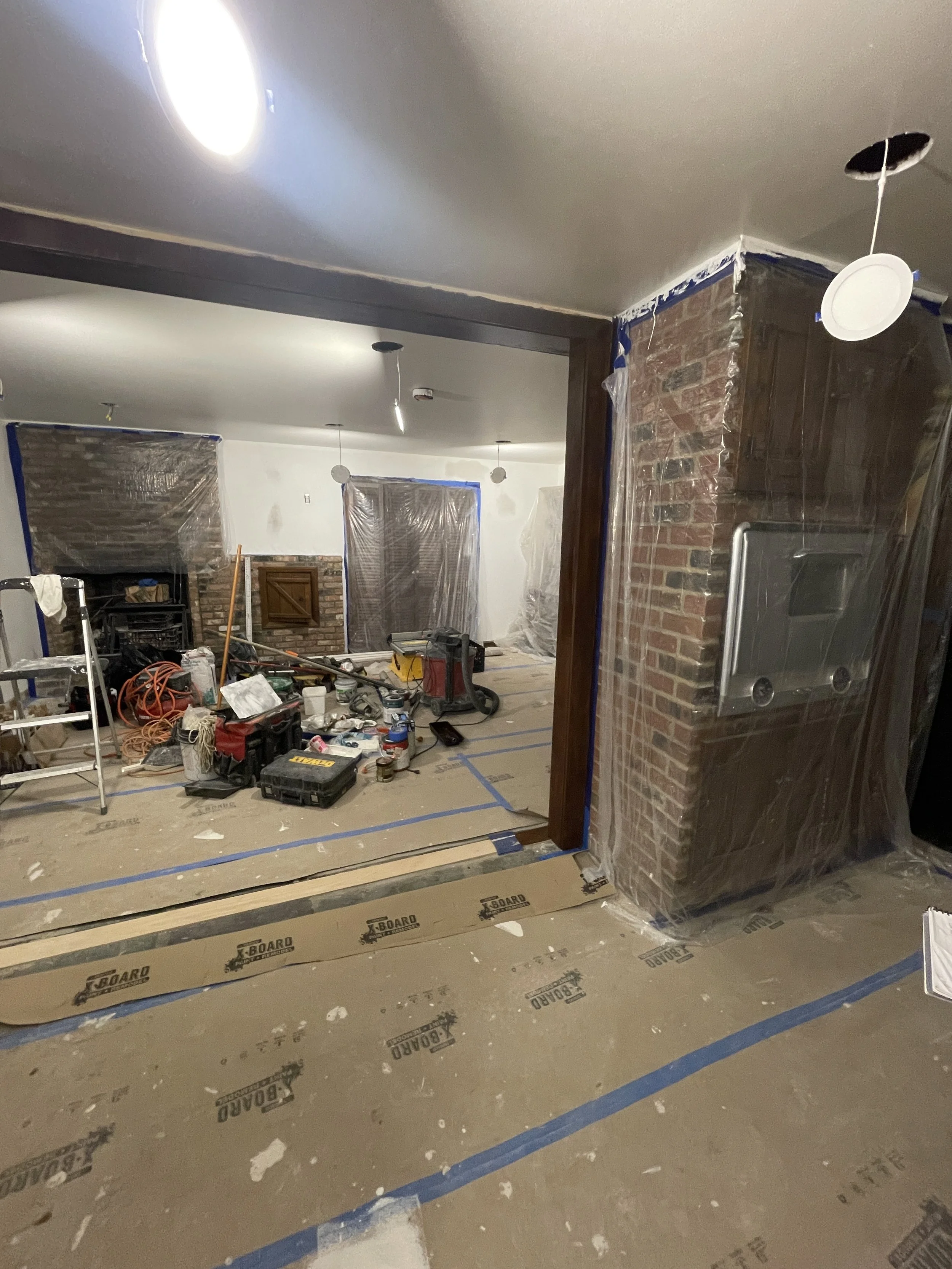 Interior of a house under renovation with tools, plastic coverings, and construction materials scattered on the floor, with brick walls and construction tape.