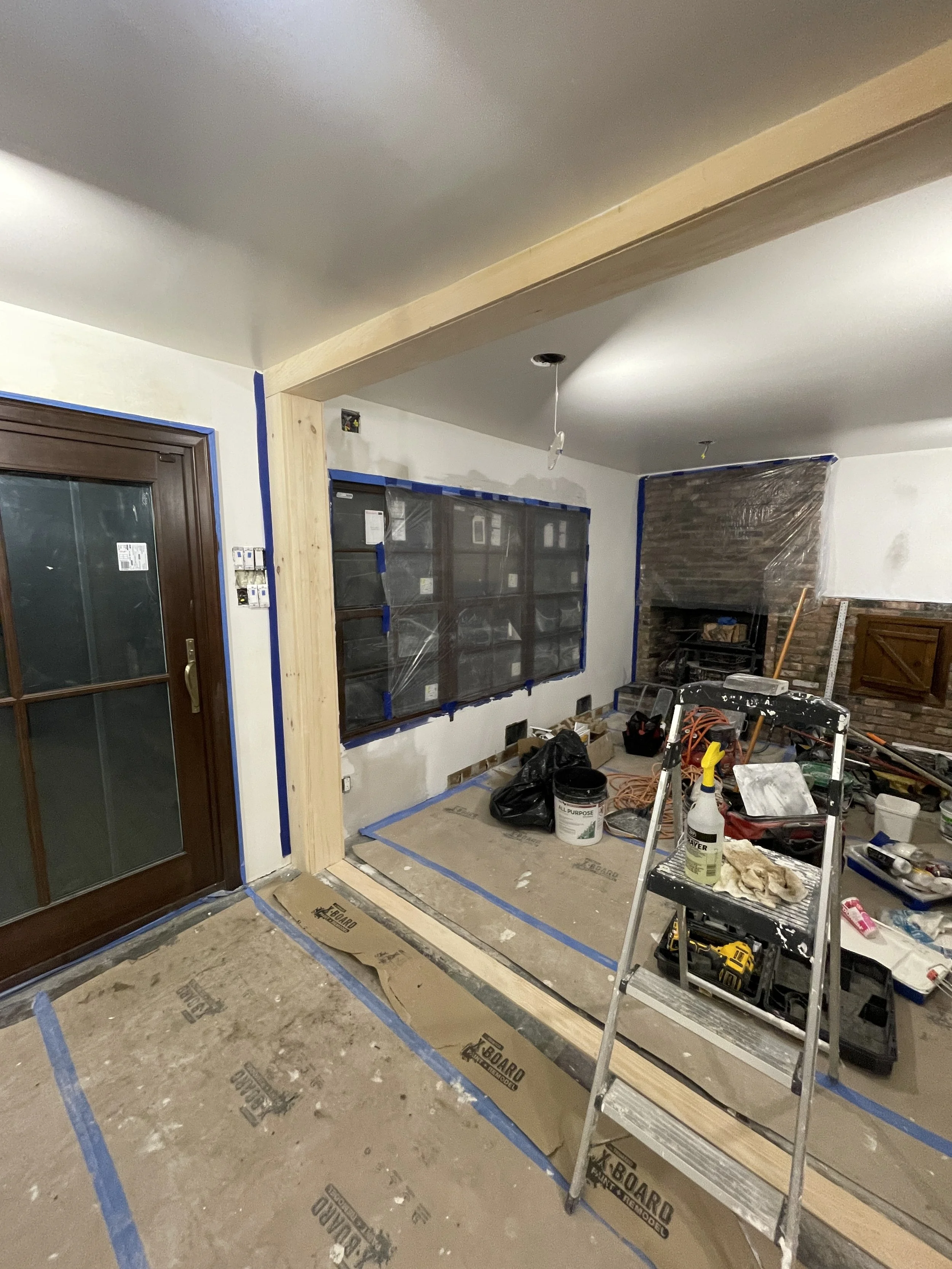 Interior of a room under renovation with tools, construction materials, and plastic-covered windows.
