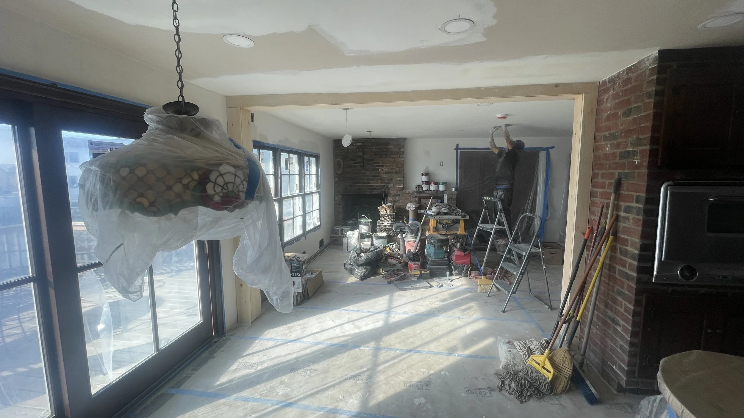 Interior of a room under renovation with construction tools, supplies, and workers installing or repairing ceiling and walls.
