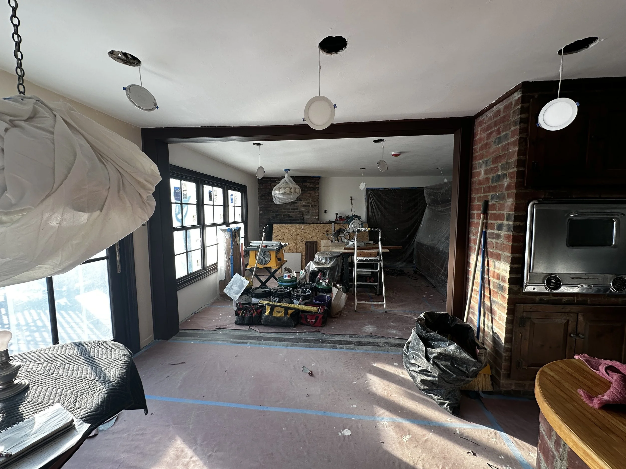 Living room under renovation with construction tools, supplies, and plastic sheeting on the ceiling and walls.