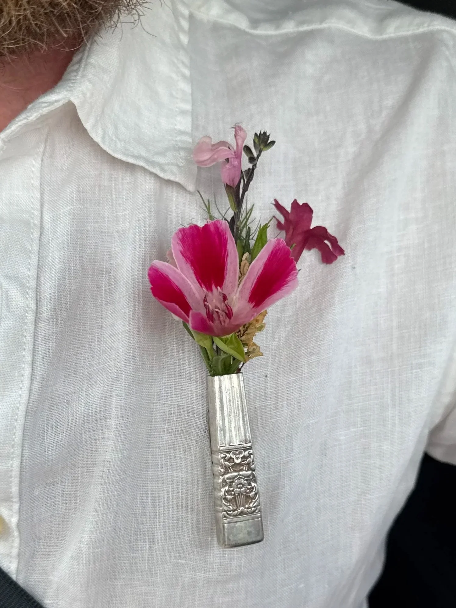 A person wearing a white shirt with a brooch holding a small bouquet of pink and purple flowers.