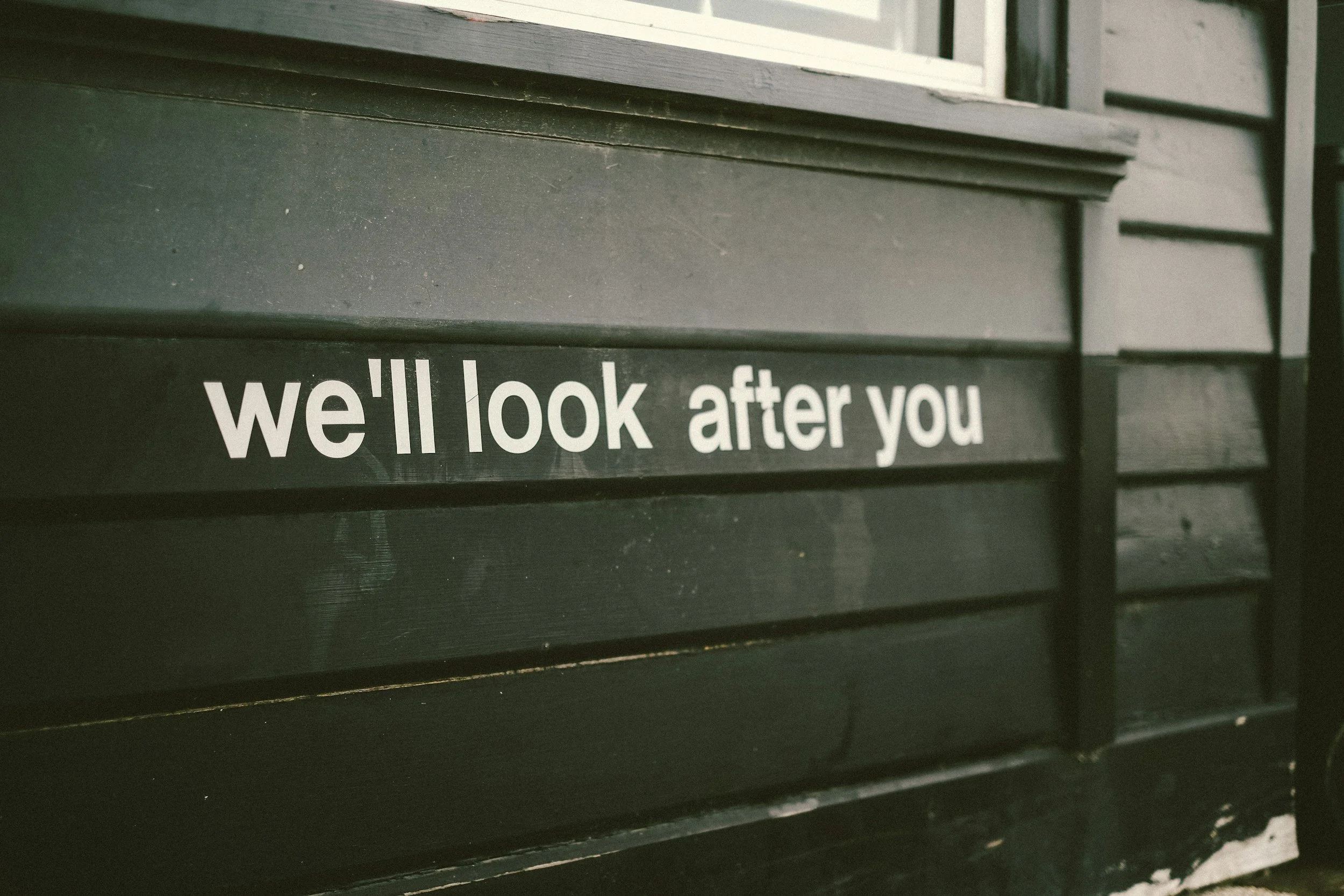 Close-up of a black mailbox with the words "we'll look after you" written in white on a strip of material attached to it.