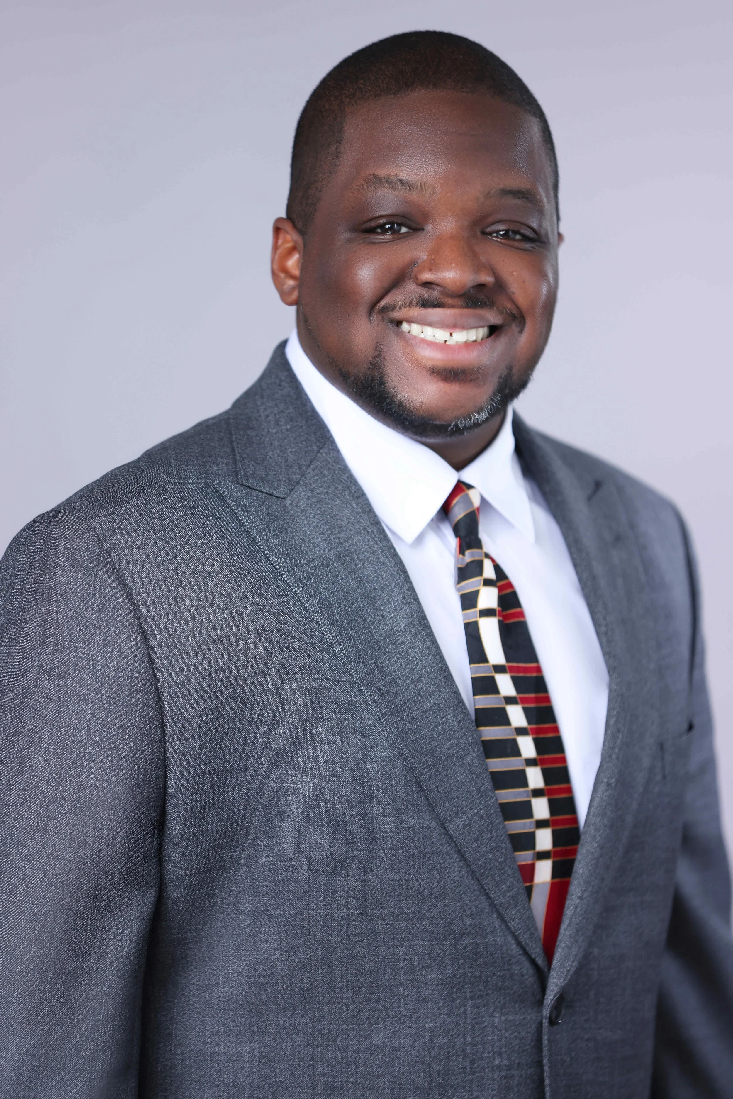 A photo of Attorney Aikeem Cooper. He is wearing a grey suit with a white shirt and a patterned tie.