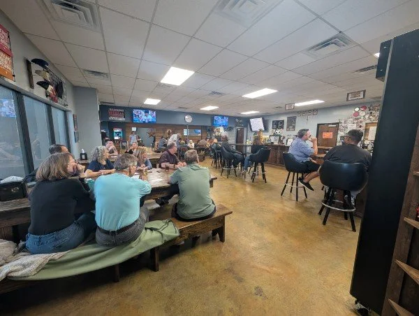 People sitting and socializing inside a casual restaurant or bar with a bar counter, multiple TVs, and a cozy ambiance.