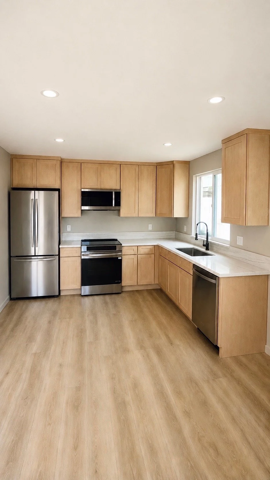 Modern kitchen with wooden cabinets, stainless steel refrigerator, stove, microwave, dishwasher, marble countertops, and a window above the sink.