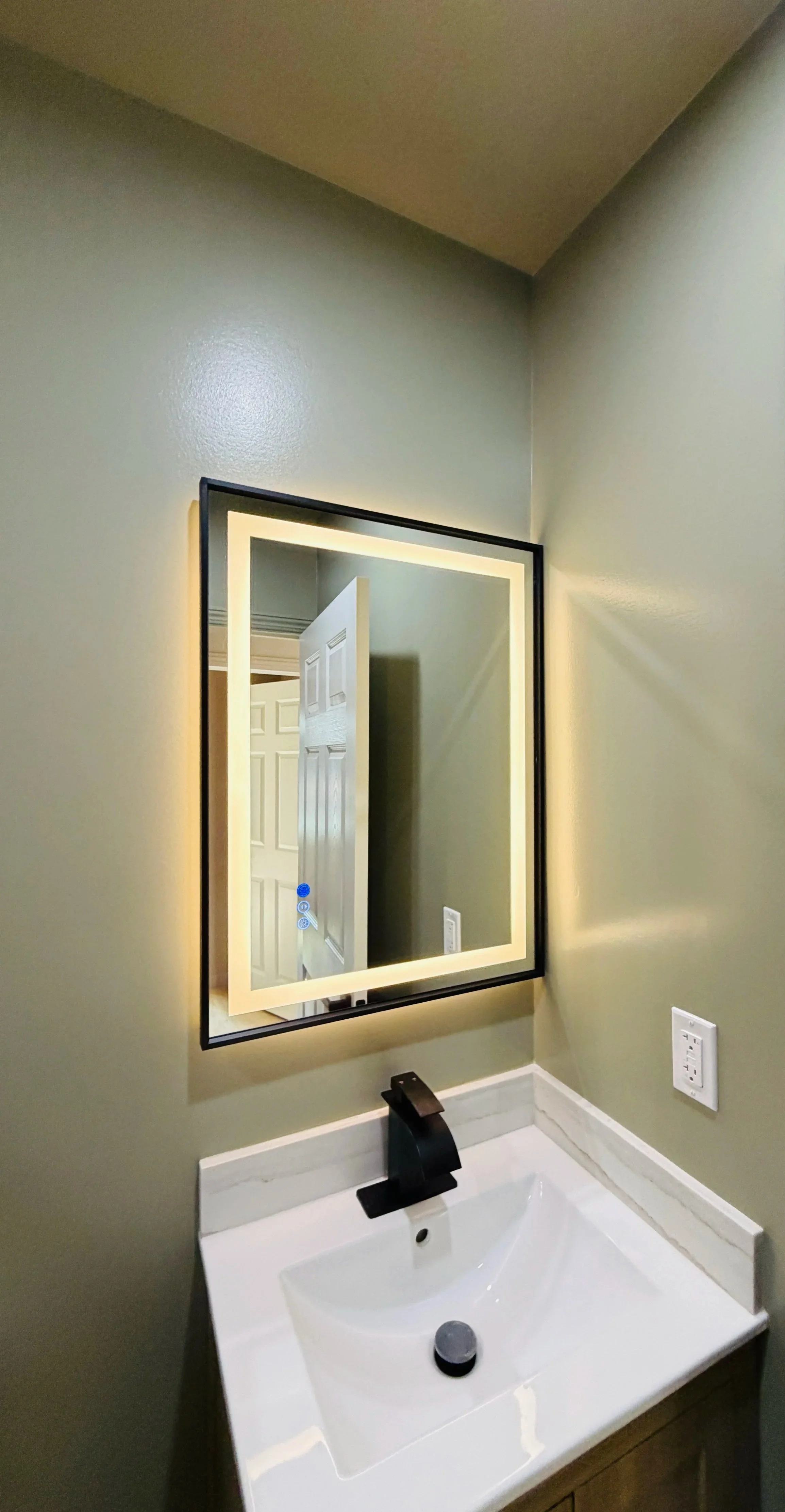 A bathroom vanity with a white sink, black faucet, wall-mounted mirror with backlight, and a green wall.