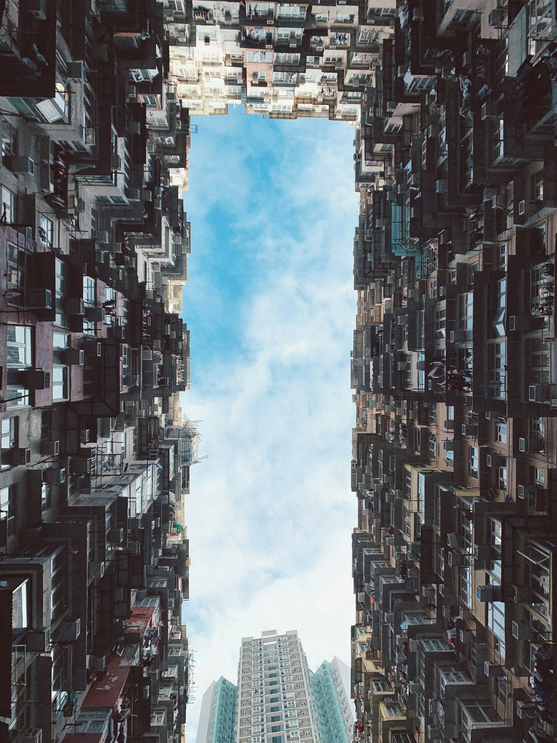 View from the ground looking up at tall apartment buildings with a blue sky in the center.
