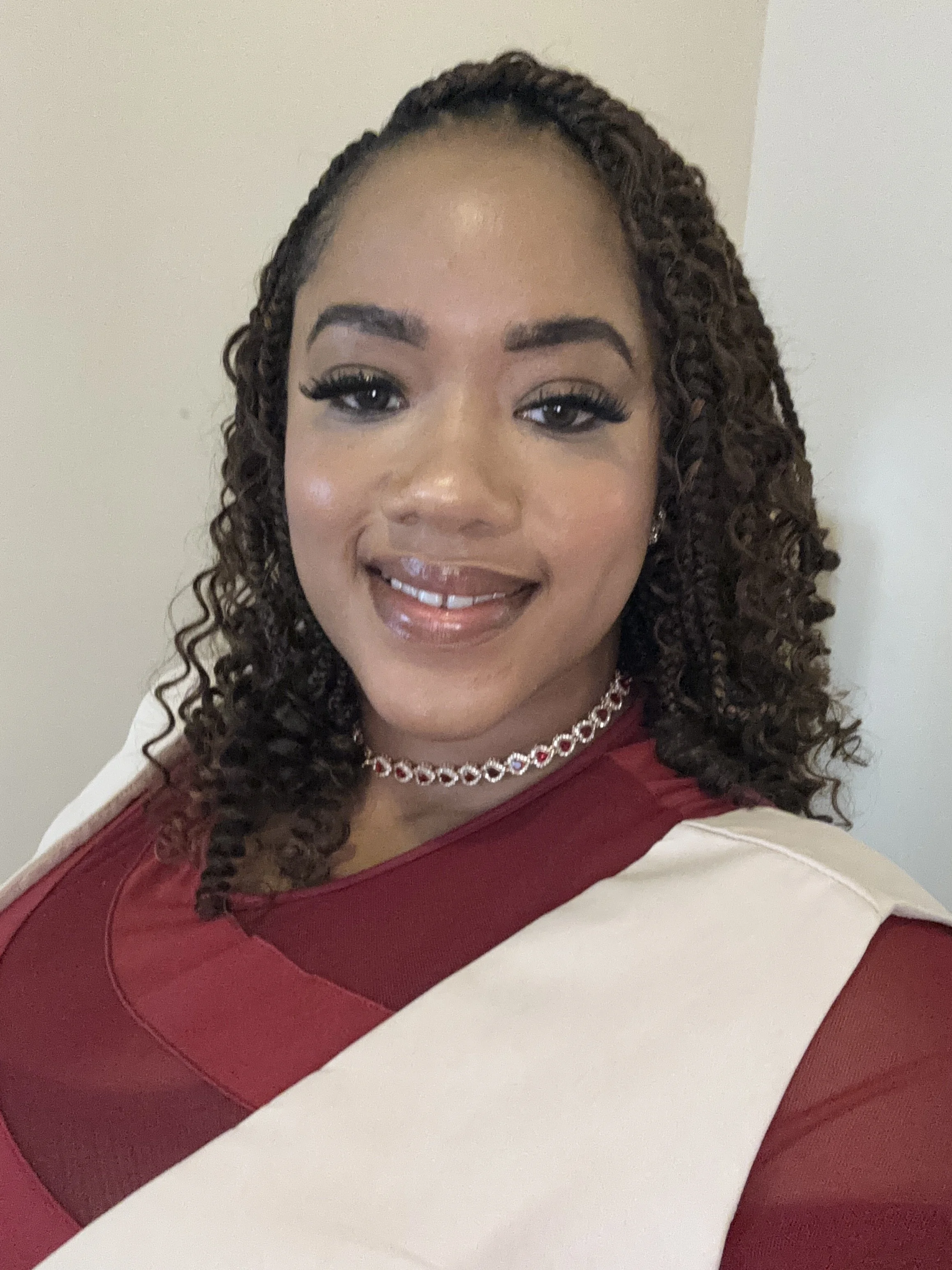 A woman with curly hair, wearing a red and white top, and a necklace, smiling at the camera.