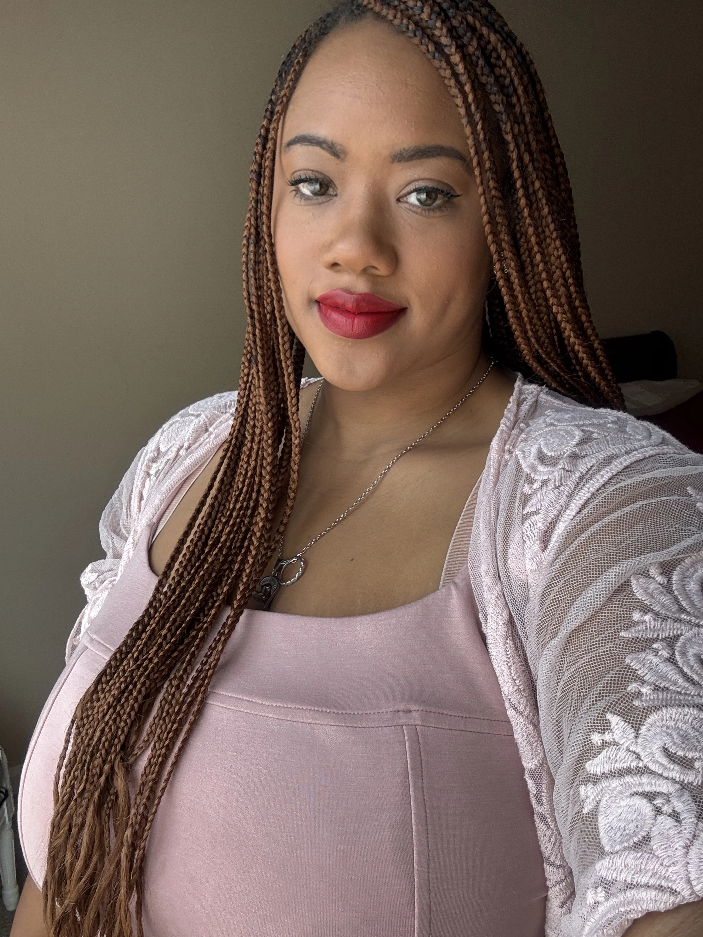 Close-up of a woman with long braided hair, wearing a pink top with lace sleeves, and red lipstick.