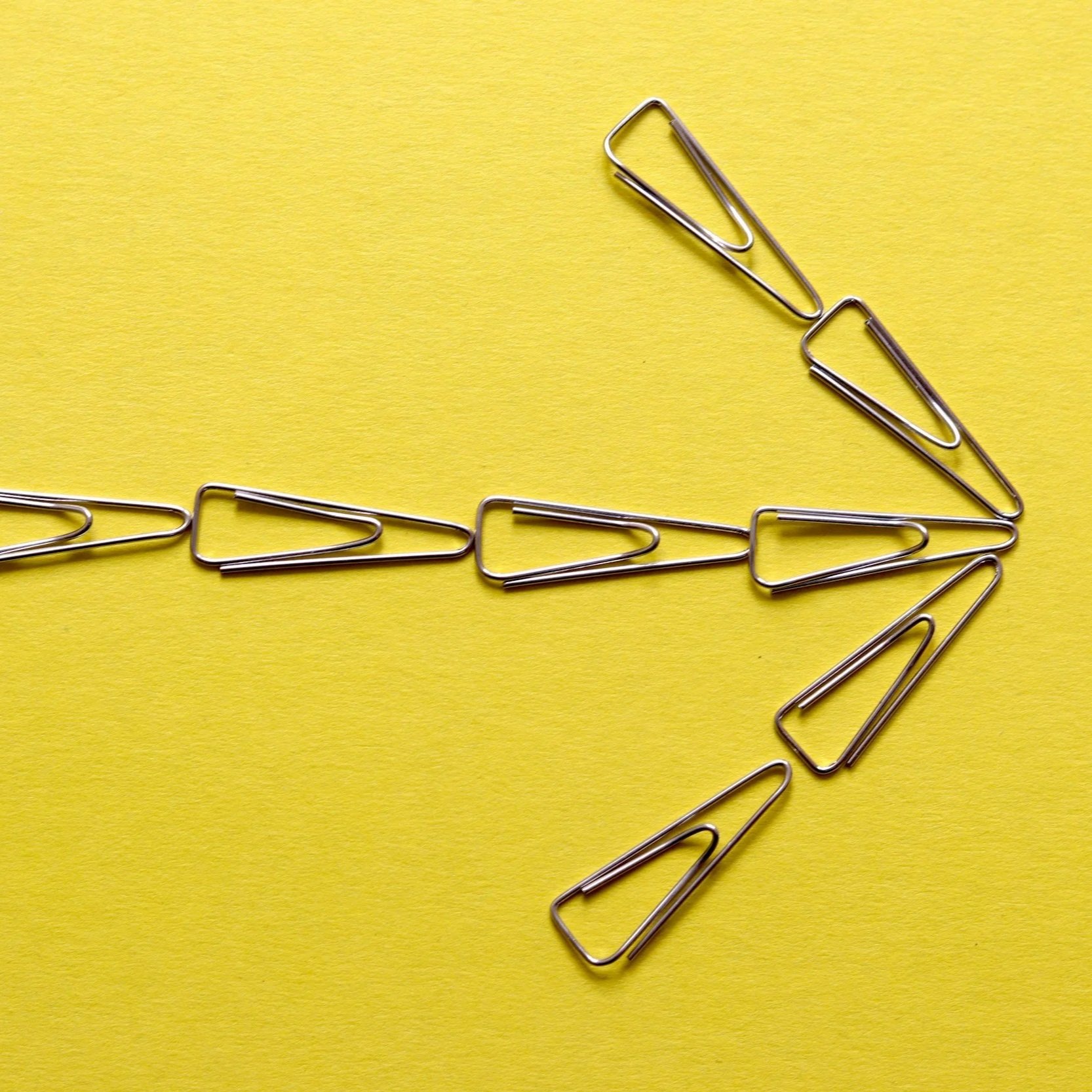 A chain of paper clips arranged in a zigzag pattern on a yellow background.