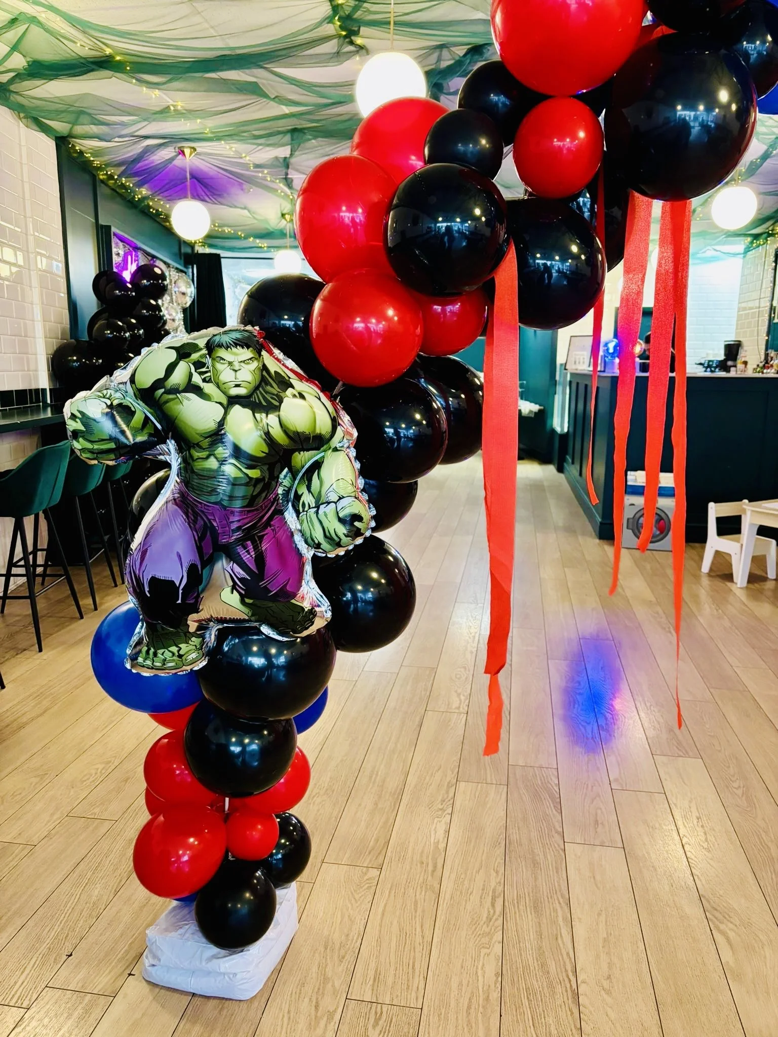 A decorative display with black, red, and a few purple balloons on a wooden floor, topped with a balloon shaped like the Hulk.
