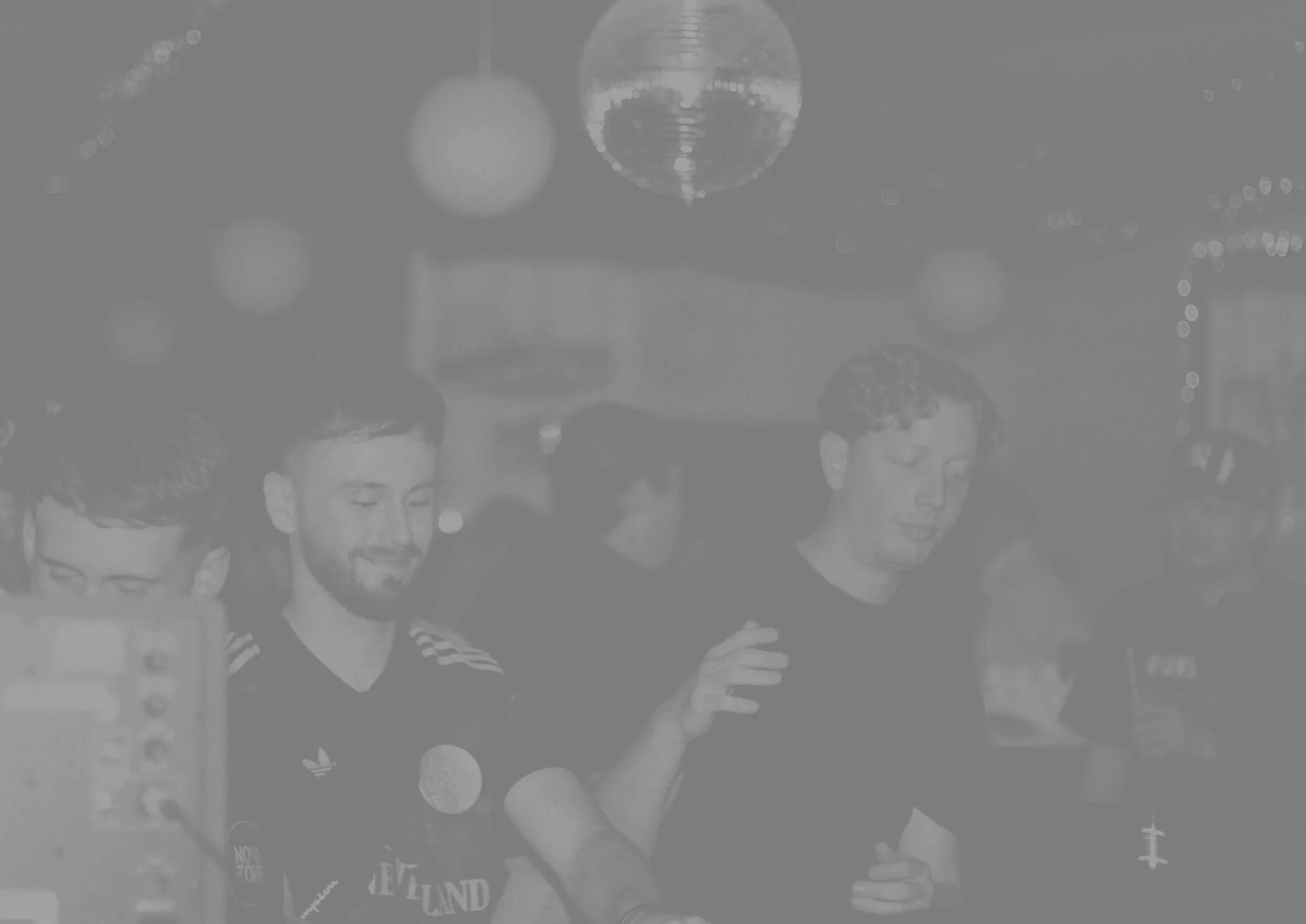 A group of young men, possibly friends, standing together at what appears to be a party or celebration. They are dressed casually, some holding drinks, and the background features hanging disco balls and decorative lights, indicating a festive atmosphere.