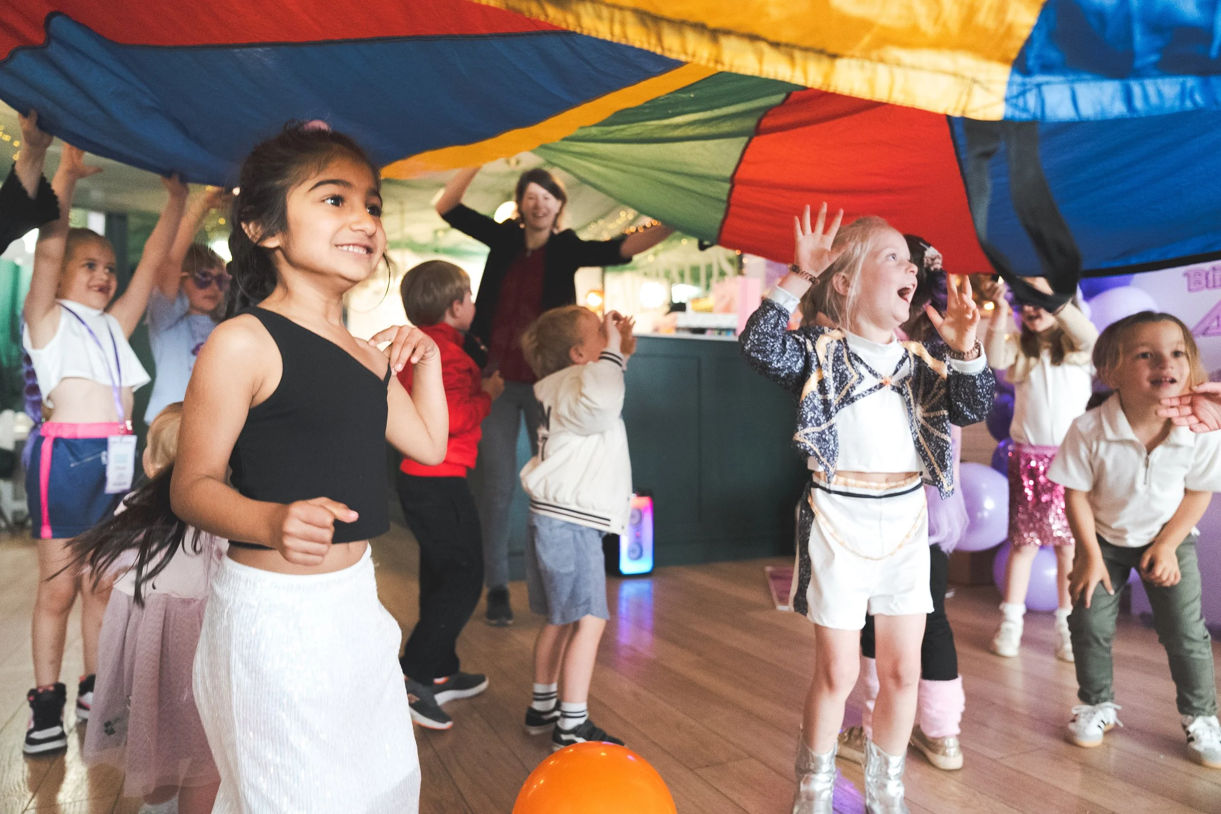Children playing under a multicolored parachute at a party or event.