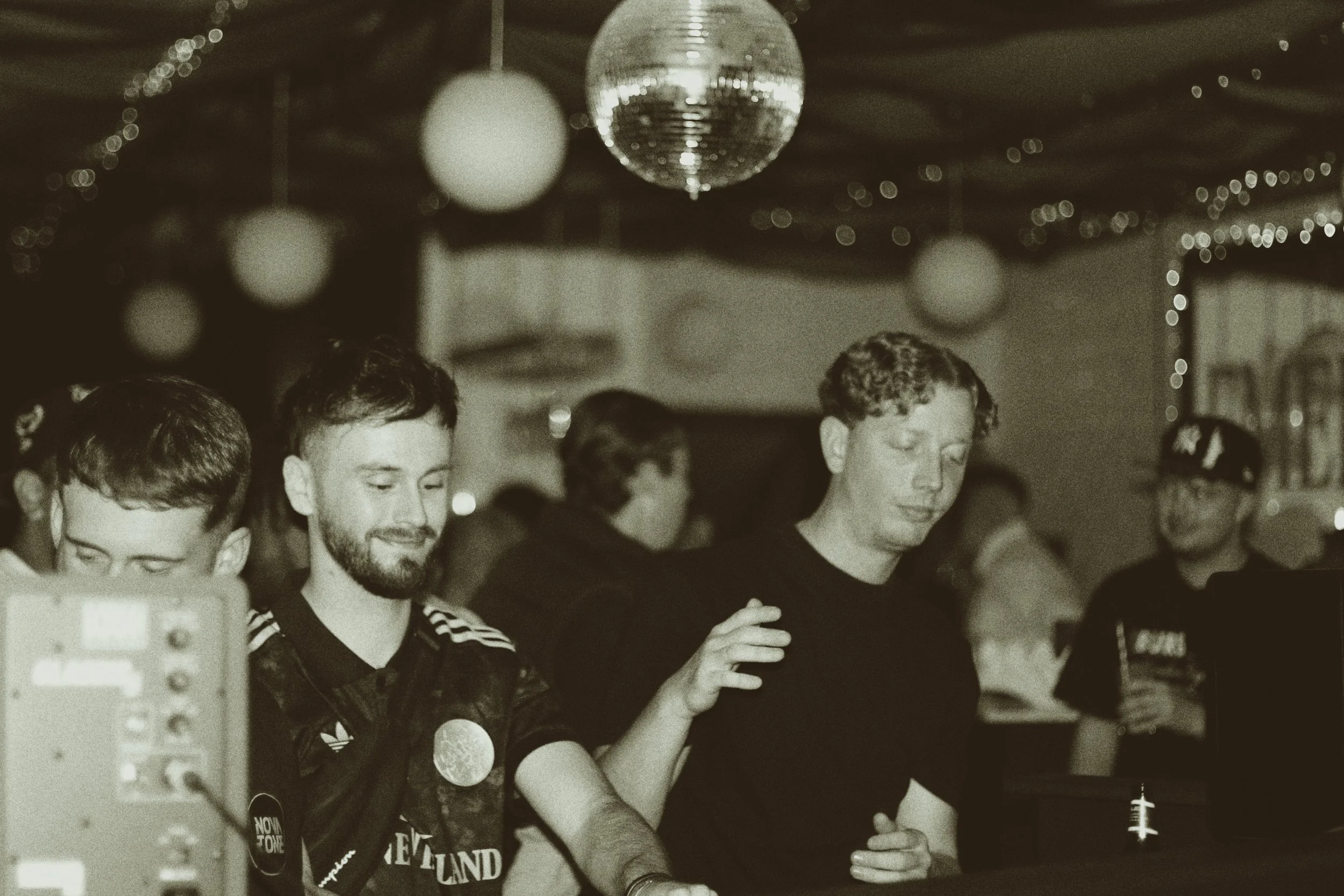 A group of young men gathered at a party, with a disco ball hanging from the ceiling and string lights in the background. They appear to be socializing and enjoying themselves.